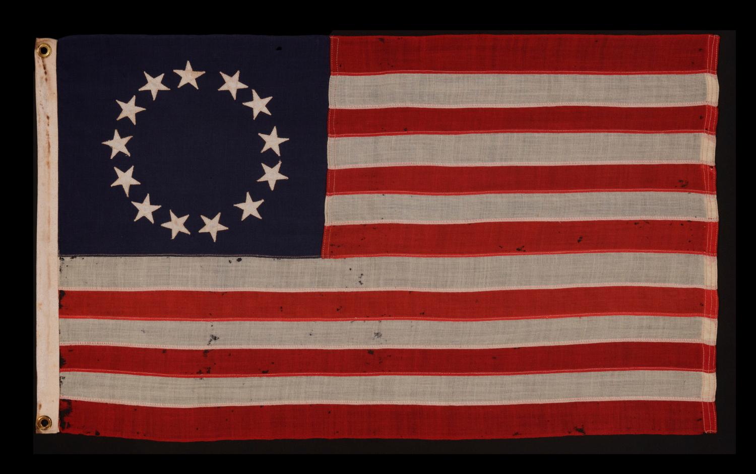 13 STARS IN THE BETSY ROSS PATTERN ON A SMALL-SCALE ANTIQUE AMERICAN FLAG OF THE 1895-1920’s ERA 

13 star flag of the type made from roughly the last decade of the 19th century through the first quarter of the 20th. The stars are arranged in the