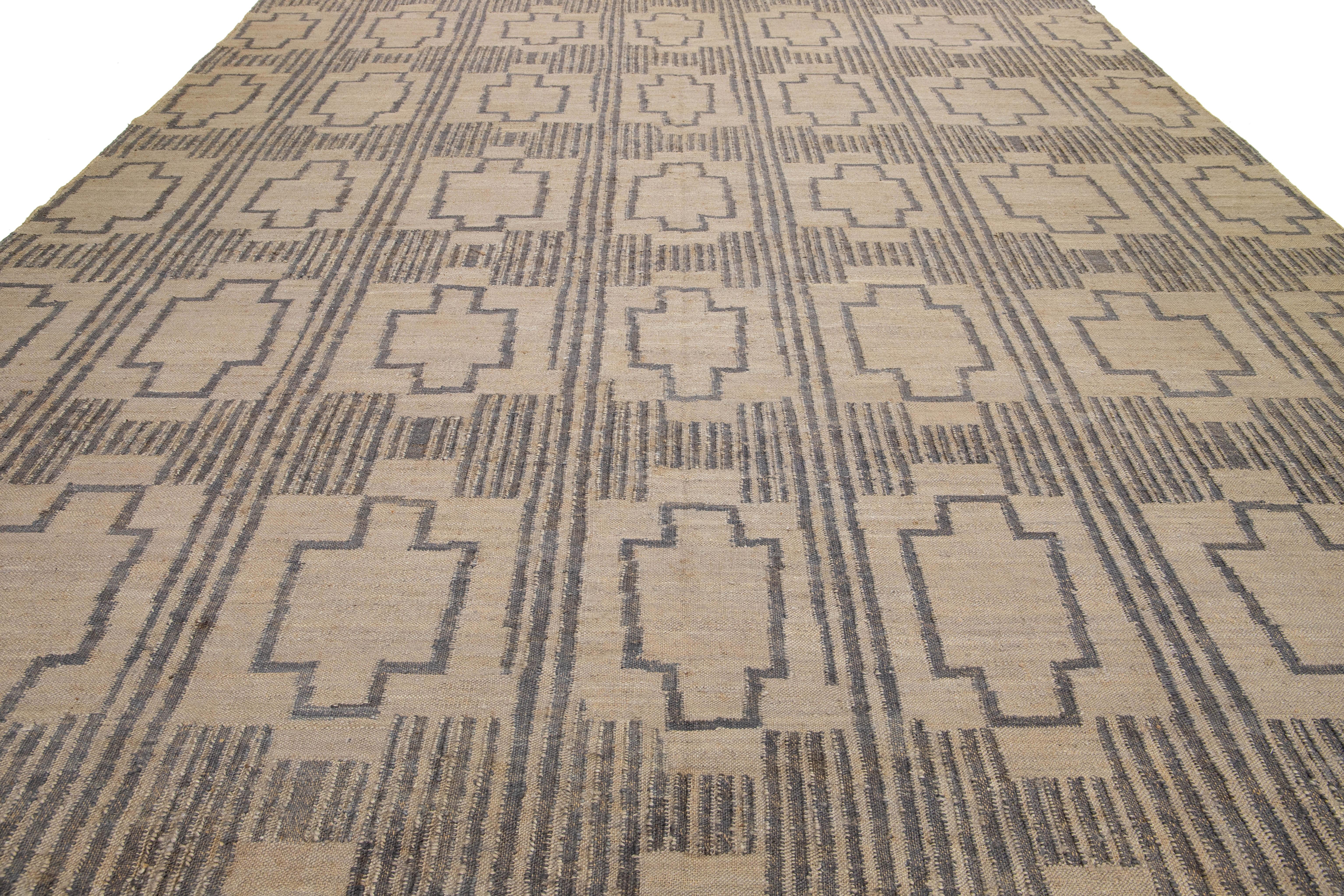 This flatweave natural jute rug showcases a contemporary Dhurrie design, featuring a tan-beige base color and stylish gray geometric accents.

 This rug measures 12'9