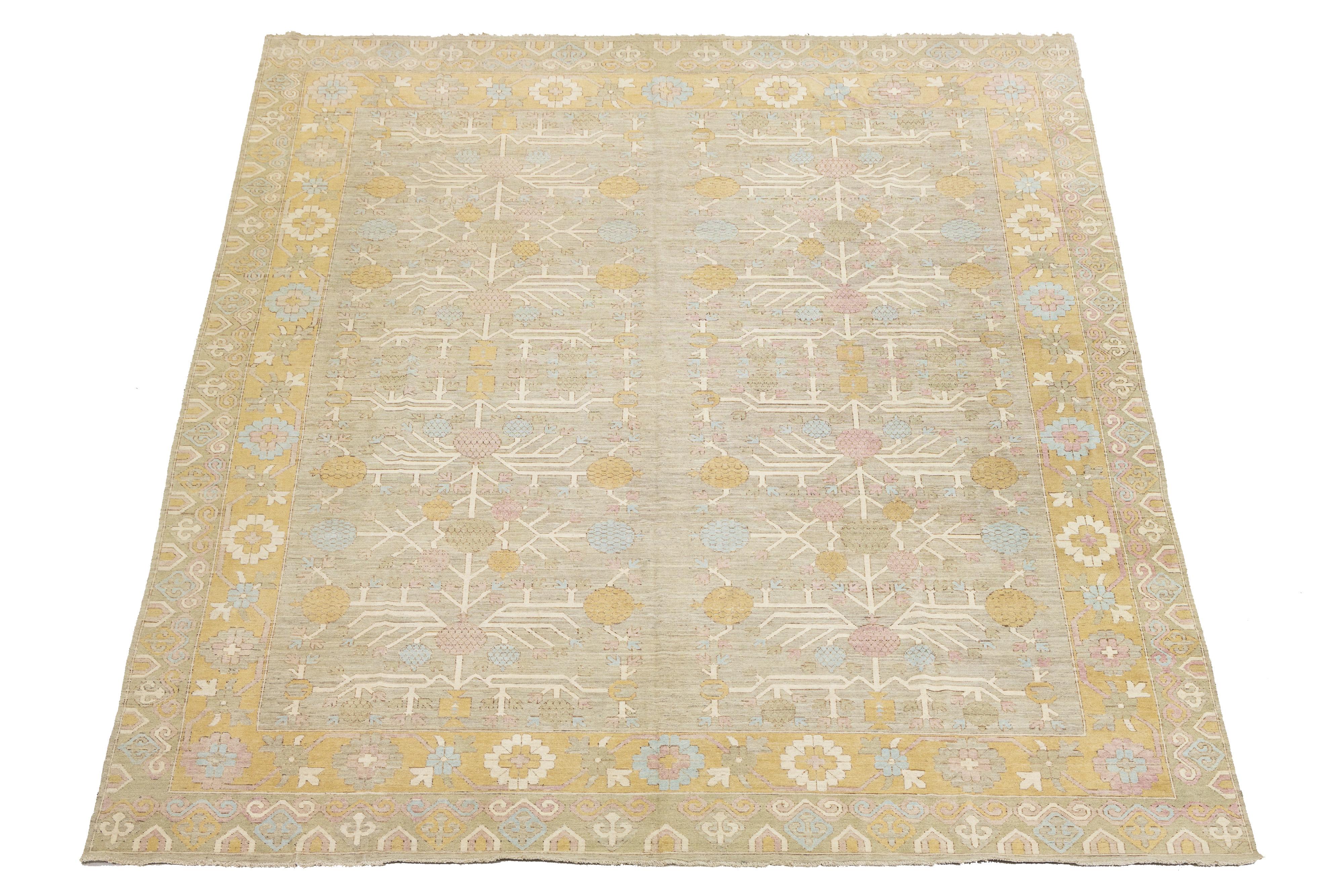 Ce tapis en laine noué �à la main dans le style Khotan présente un champ beige chaud joliment rehaussé de touches de verge d'or, de rouge et de bleu. Son design présente un motif complexe d'emboîtement sur tout le pourtour, mêlant harmonieusement des