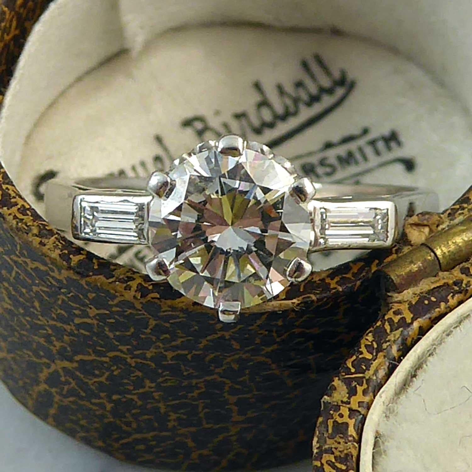 A fabulous simple and elegant solitaire engagement ring set with a brilliant cut diamond 1.10ct in a six white prong setting to a decorative mount.  The diamond is assessed as J/K colour and SI2 clarity.  The shoulders are each set with a baguette