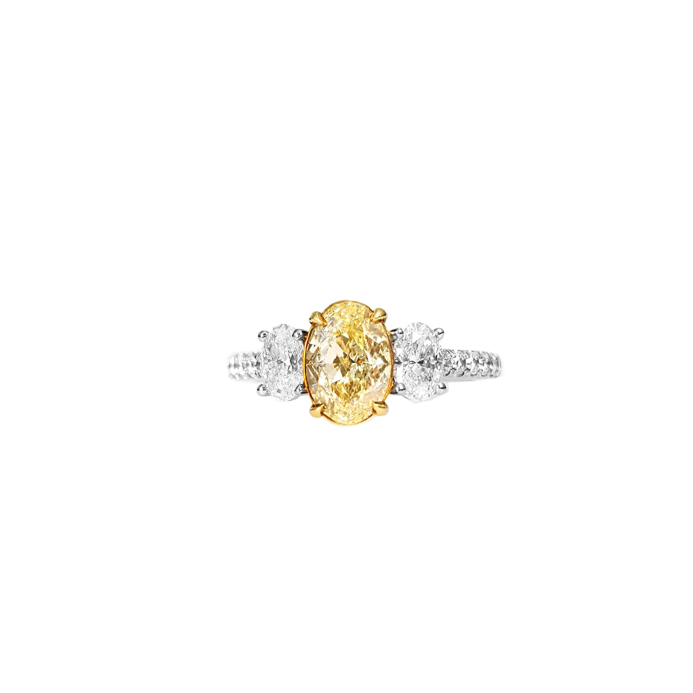 Presenting an exquisite Three-Stone Engagement Ring showcasing a 1.30-carat Fancy Yellow, oval-cut diamond. GIA certified this diamond as VS1 in clarity. The stones exhibit an excellent polish and a Very Good symmetry, ensuring a dazzling and
