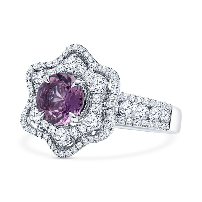 A beautiful round purple-pink sapphire weighing 1.30 carats total sets the stage for this beautiful ring. It is accented by 1.39 carat total weight in round diamonds in a double halo floral pattern with additional diamonds halfway down the band and