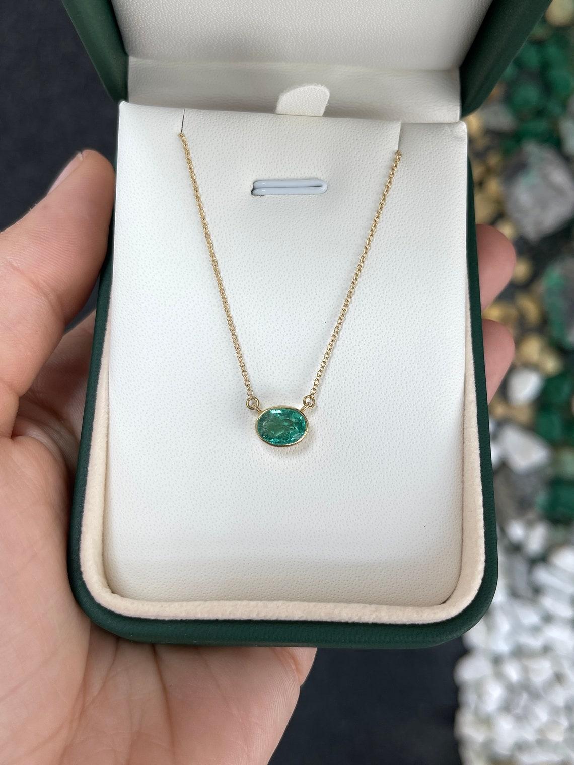 Introducing a captivating solitaire emerald necklace, adorned with a breathtaking 1.30-carat oval cut emerald. Set horizontally in a thin bezel setting, the emerald showcases a medium green color, with semi-transparent clarity and a delightful play