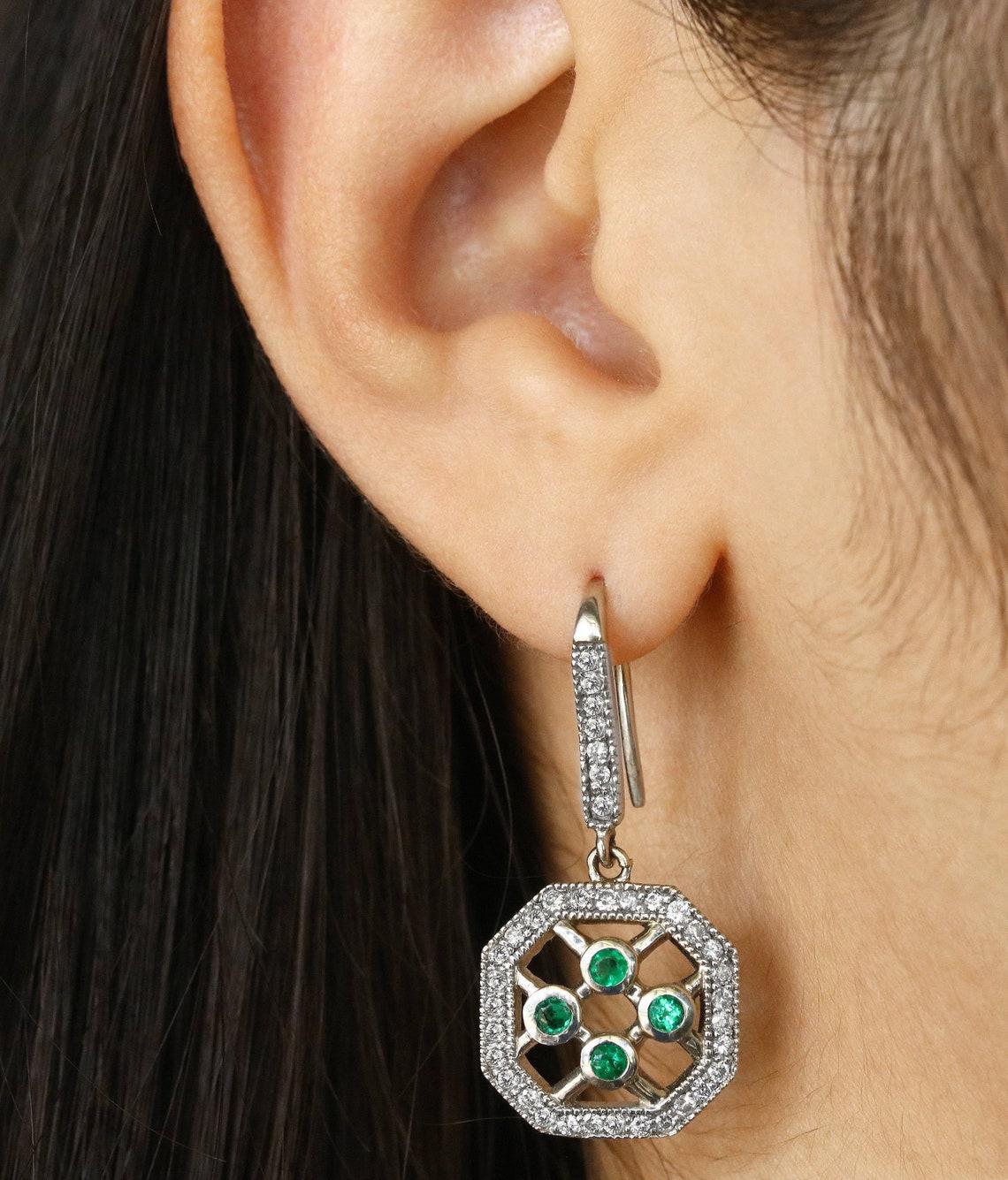 An impressive pair of Colombian emerald and diamond french hook earrings. Crafted in 14K white gold, numerous emeralds are handset in a gold bezel setting. The emeralds are all earth-mined and have a bright bluish-green color to them. Excellent