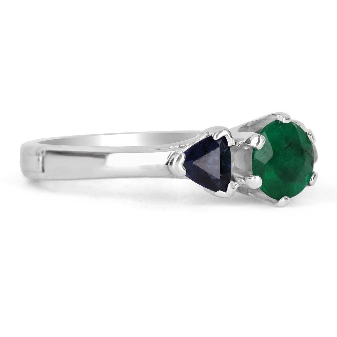 Displayed is a classic three stone ring with emerald and blue sapphire. This gorgeous ring carries a full 0.75-carat emerald in a six-prong setting. Fully faceted, this gemstone showcases excellent shine. The emerald has very good clarity with minor