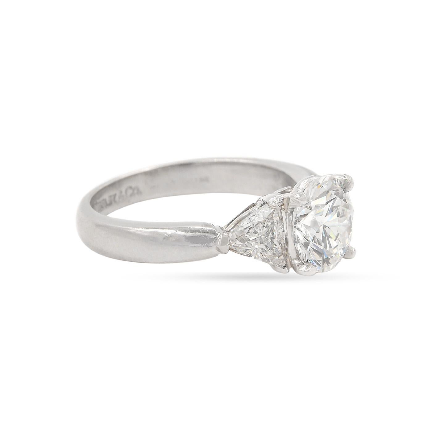 A classic 3-Stone engagement ring by Tiffany & Co. composed of platinum. Featuring a 1.31 Carat Round Brilliant Cut Diamond, GIA certified F color & VVS2 clarity. Flanked by 2 Trilliant Cut diamonds set on the shoulders, weighing approximately 0.61