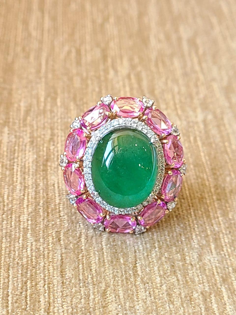 A very gorgeous and one of a kind, Emerald & Pink Sapphires Cocktail Ring set in 18K Gold & Diamonds. The weight of the Emerald Cabochon is 13.18 carats. The Emerald is of Zambian origin and is completely natural, without any treatment. The weight