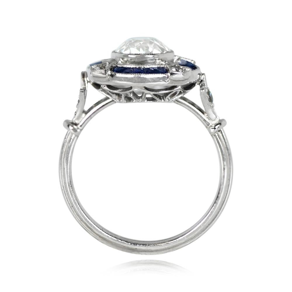 This exquisite Art Deco-inspired engagement ring showcases a central old European cut diamond, encircled by a halo of sapphires and diamonds. The ring is adorned with a triple wire shank and delicate fleur-de-lis motif shoulders, studded with