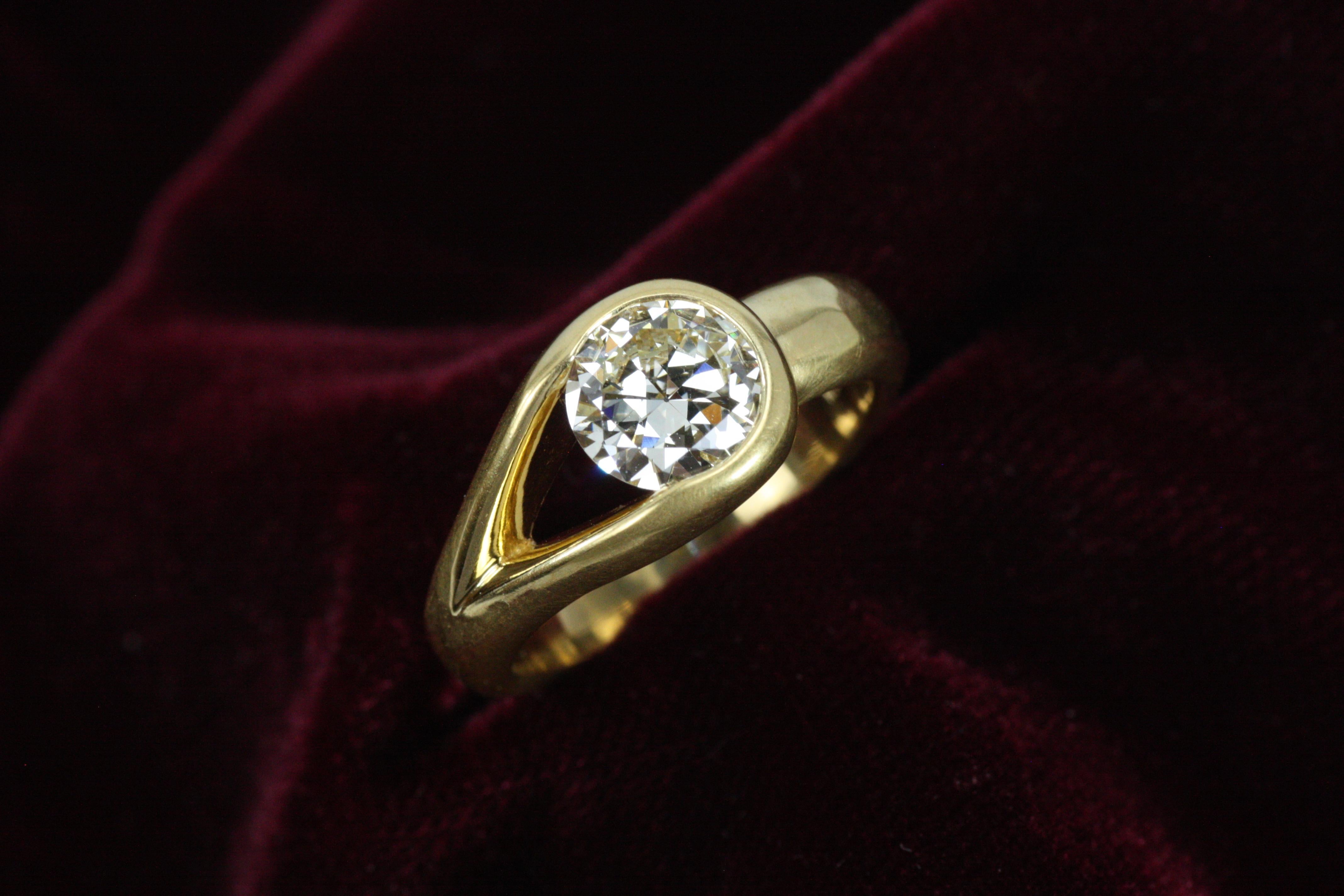 Unique asymmetrical open bezeled solitaire engagement ring featuring a 1.32 carat natural diamond in high karat 22k yellow gold. Modern and unusual, this one-of-a-kind ring boasts a matte hammered finish and tapers on one side for an organic look.