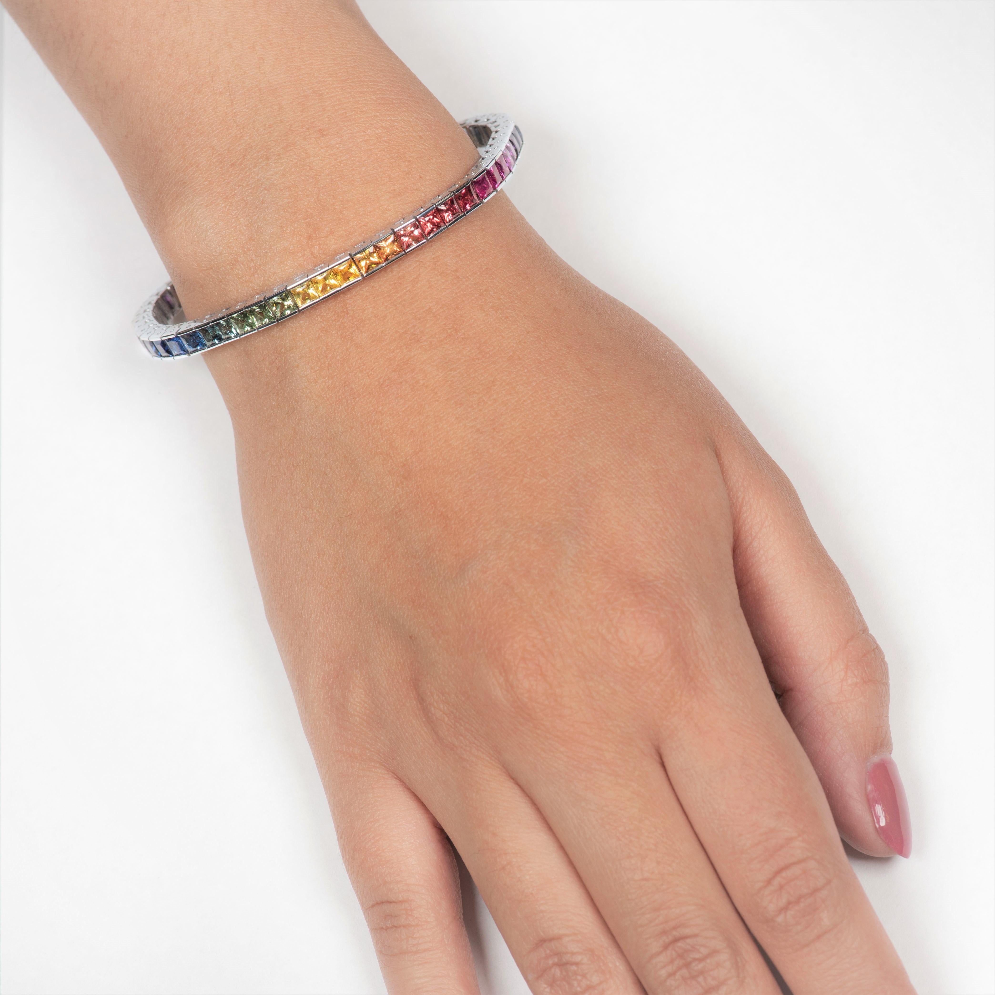 Beautifully in-house crafted channel set 14K white gold tennis bracelet that features 13.27 carats of princess cut rainbow colored sapphires. This piece is an absolute favorite as it presents 50 different colors of hue and tones of multi-colored