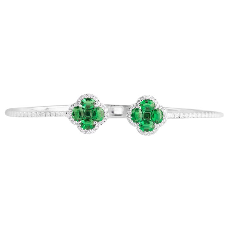 The heads on this bangle are formed by two clusters of 10 emeralds. Each head is a clover formed by four oval cut and one square cut emerald. Each clover is wrapped in a tight halo of round white diamonds, which also extends to the halfway point of