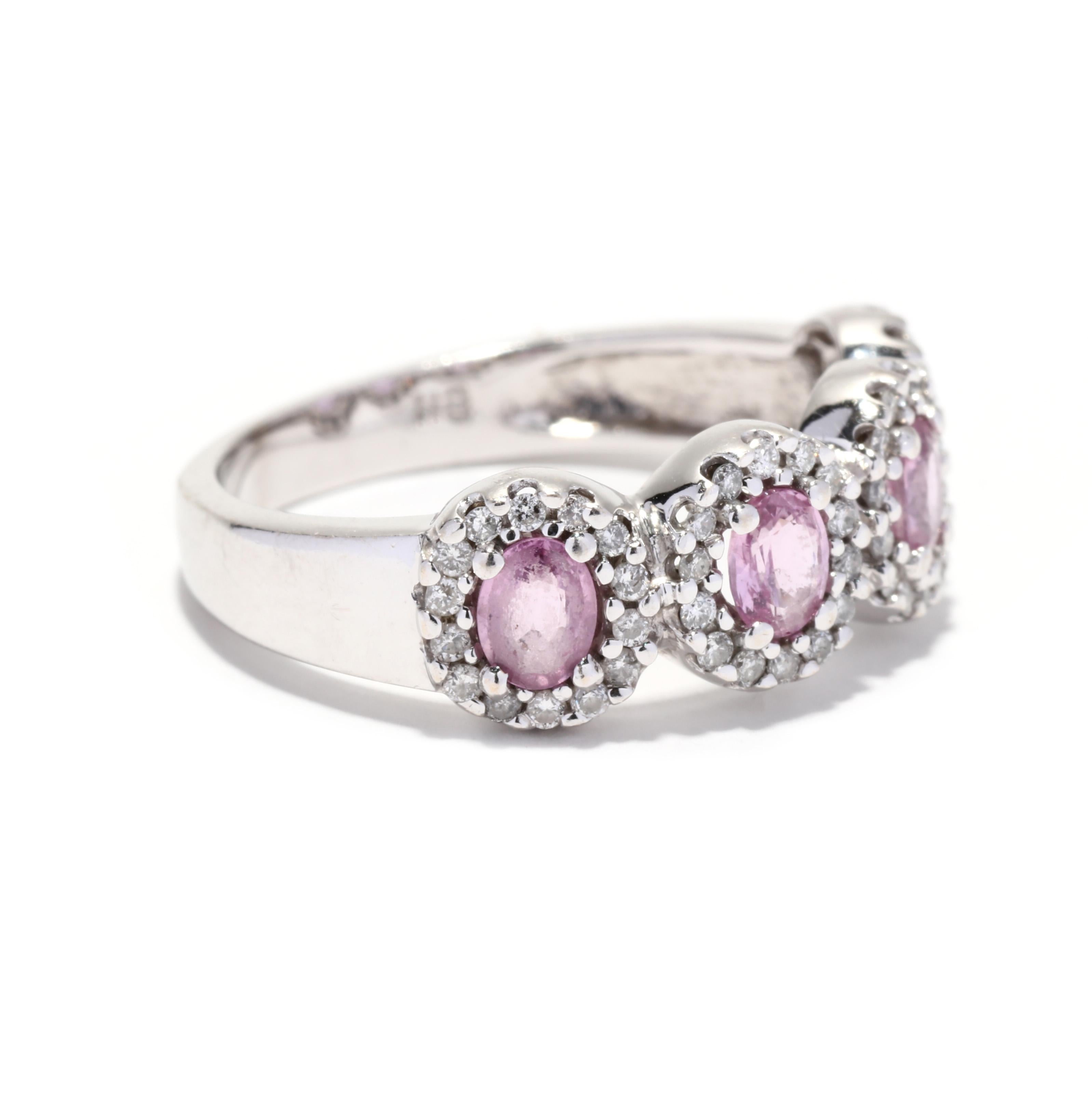 A vintage 14 karat white gold pink sapphire and diamond four stone halo band ring. This wide band features four oval cut pink sapphires weighing approximately 1 total carat, each surrounded by halo of full cut round diamonds weighing approximately