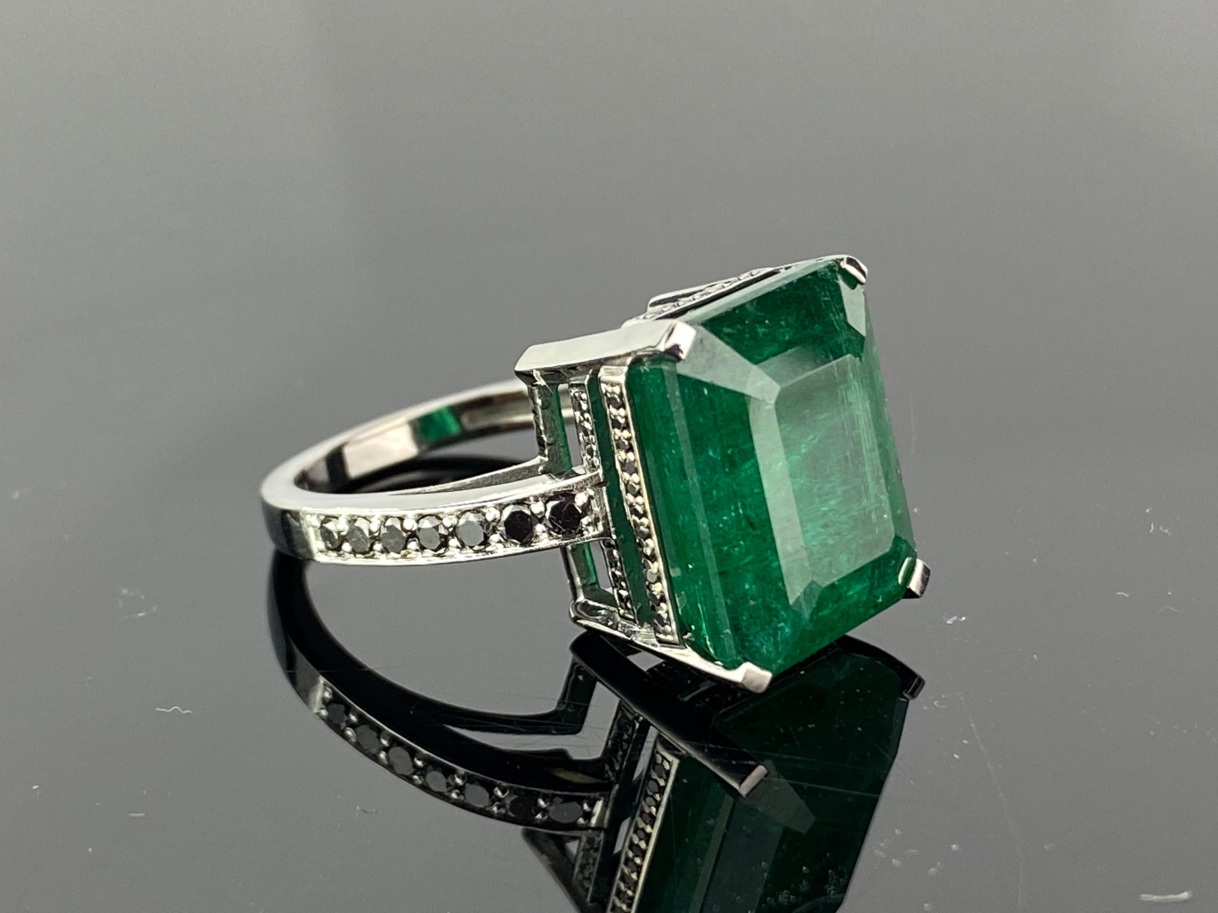 A unique 13.34 carat Zambian Emerald cocktail ring, with Black Diamonds set on the band - this ring is made in 18K Gold, which is black rhodium polished. Currently a ring size US 6, but we can resize the ring for you without additional cost. A video
