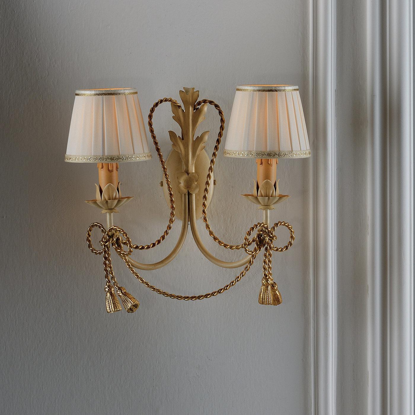 Decorate a mano in modo unico e con dettagli in foglia d'oro, entrambe le lampade di questa doppia lampada a stelo hanno un paralume in tessuto color avorio. Questo pezzo elegante è unito da un cavo di metallo dorato legato in un fiocco alla base di