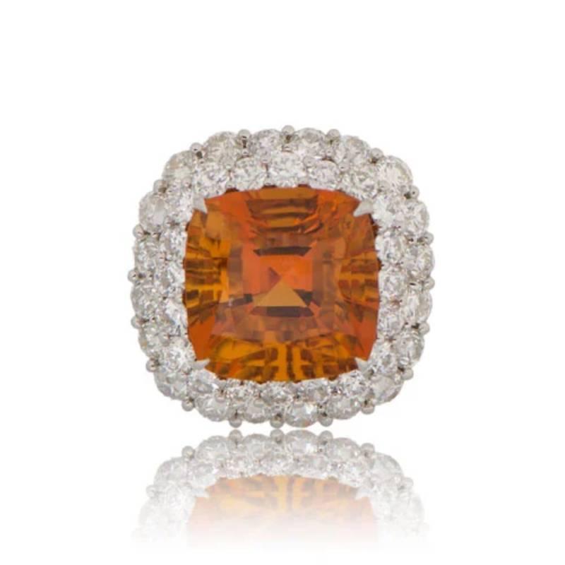 A stunning citrine cocktail ring featuring a 13.43-carat natural citrine set in prongs. The center stone is surrounded by a double halo of diamonds, with additional diamonds along the shoulders and lower gallery. The handcrafted platinum mounting