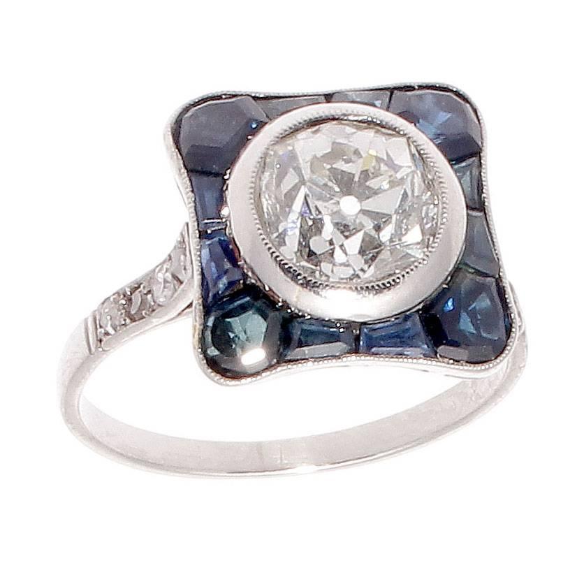 A beautiful twist on the traditional halo design. Featuring a 1.35 carat old European cut diamond that is J color, SI2 clarity. Surrounded by approximately 1.60 carats of vibrant specialty cut navy blue sapphires that perfectly fit and orbit around