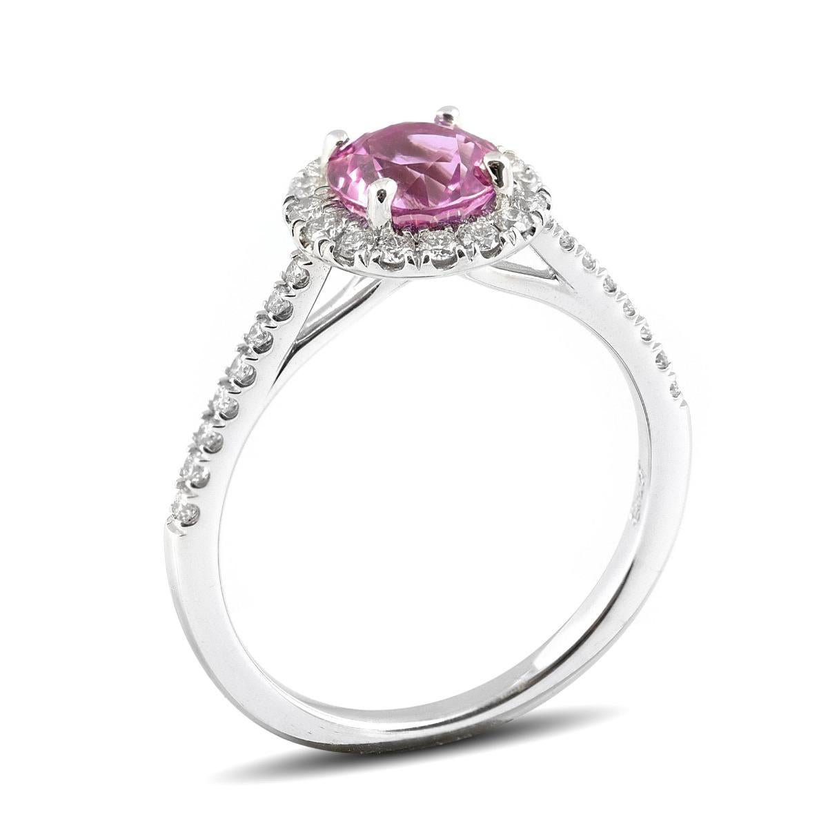 Contempla un fascinante zafiro rosa fucsia de 1,35 quilates, rodeado de un brillante halo de diamantes, que promete cautivar su corazón. La piedra, tallada en forma de brillante redondo, ostenta un color uniforme en el cuerpo que emana una