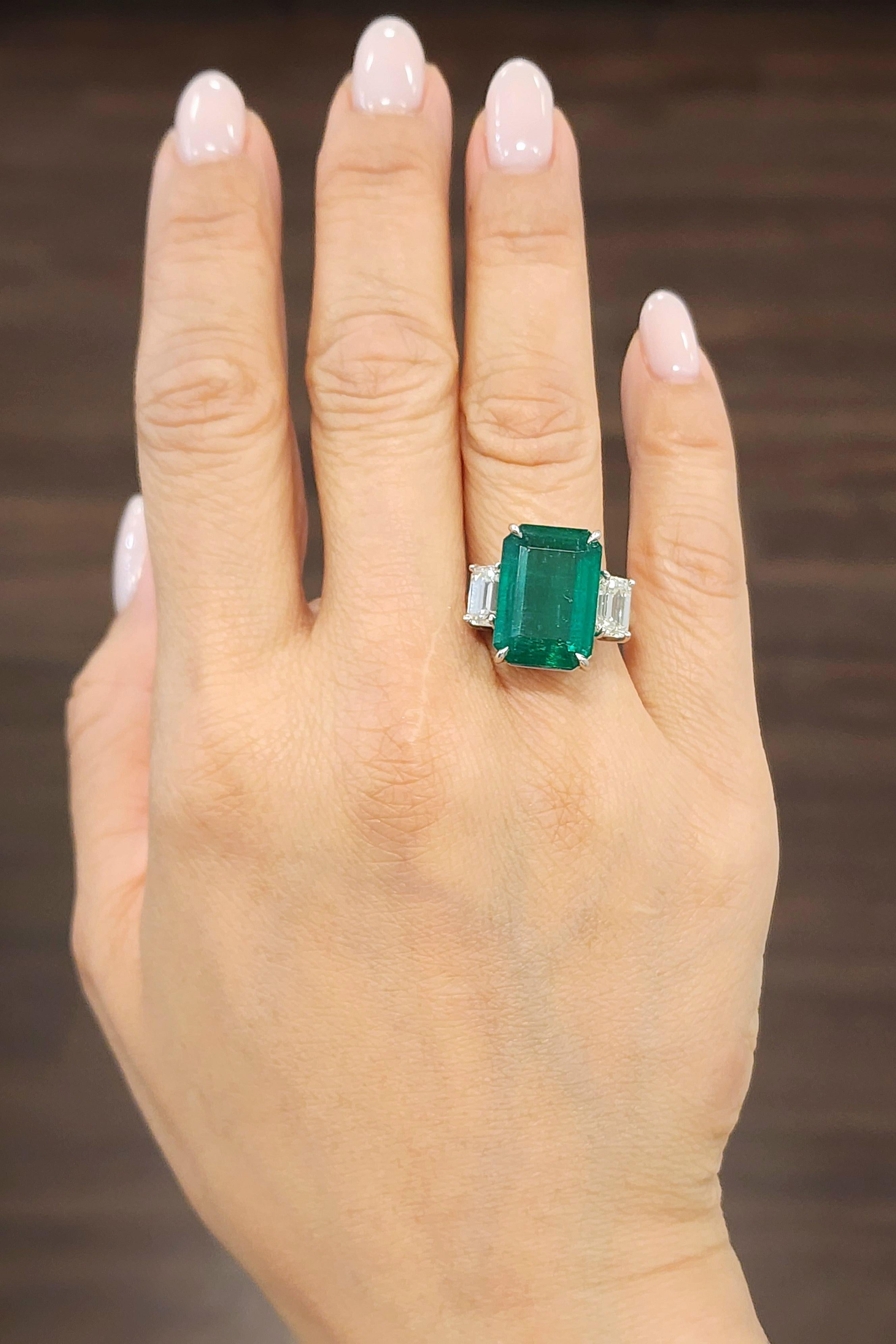 This striking platinum cocktail ring showcases a stunning 11.42 carat GIA certified emerald-cut green emerald. Flanked by two emerald-cut white diamonds totaling 2.08 carats, the diamonds possess a VS1/VS2 clarity and an I/J color grade. Crafted in