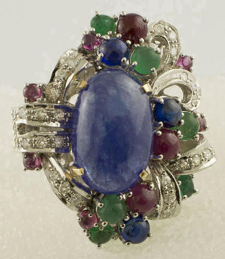 Amazing cocktail ring in 14K white gold mounted with 13.53 ct of gorgeous tanzanite in the center surrounded by white gold detailes all studded by 0.57 ct of  little white diamonds, and 6.23 ct of  cabochon cut little rubies, blue sapphires and