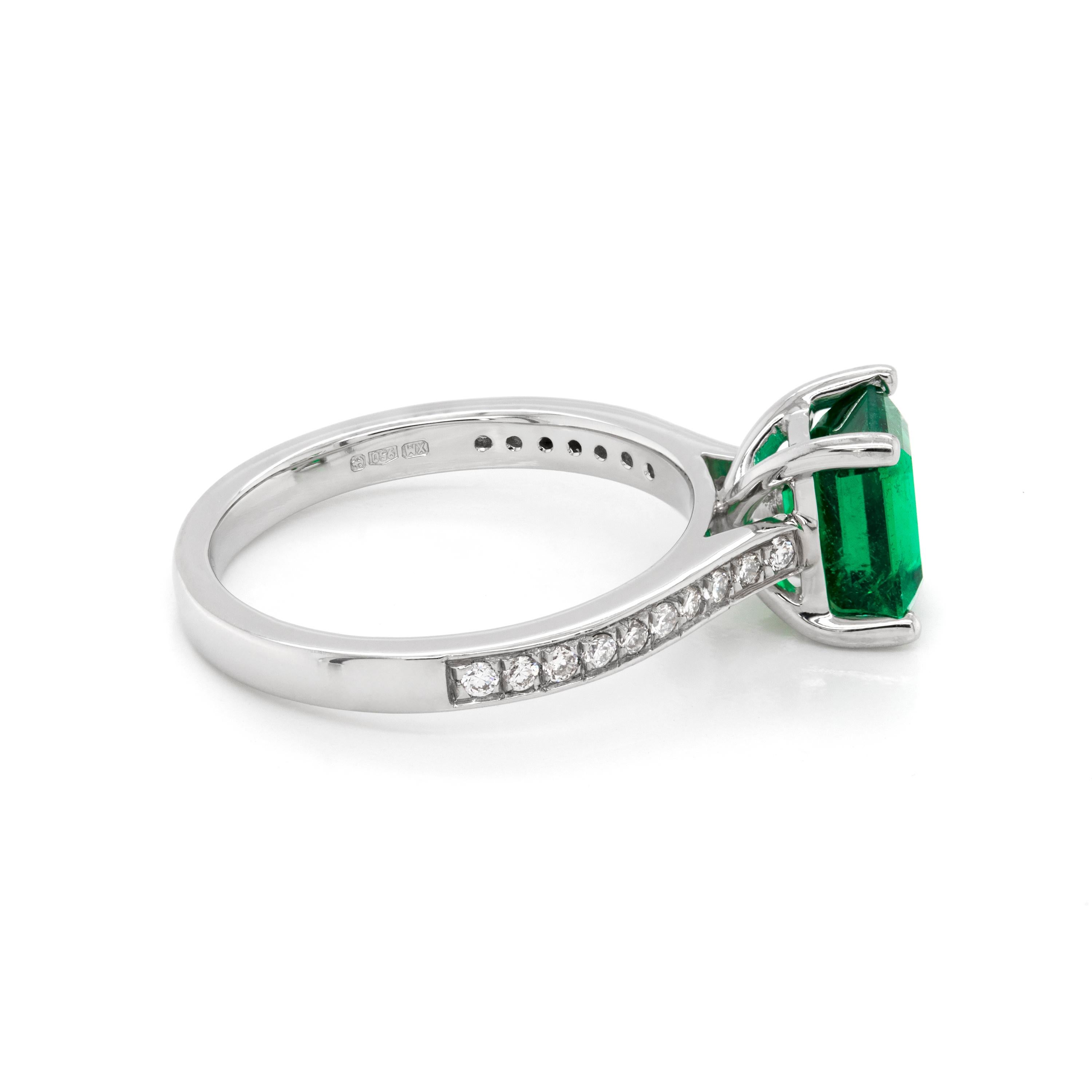 Engagement ring set with a vibrant emerald cut emerald weighing 1.36ct mounted in a four claw, open back setting. The stone is beautifully accompanied by ten round brilliant cut diamonds pavé set on either shoulder weighing a total of 0.15ct, all