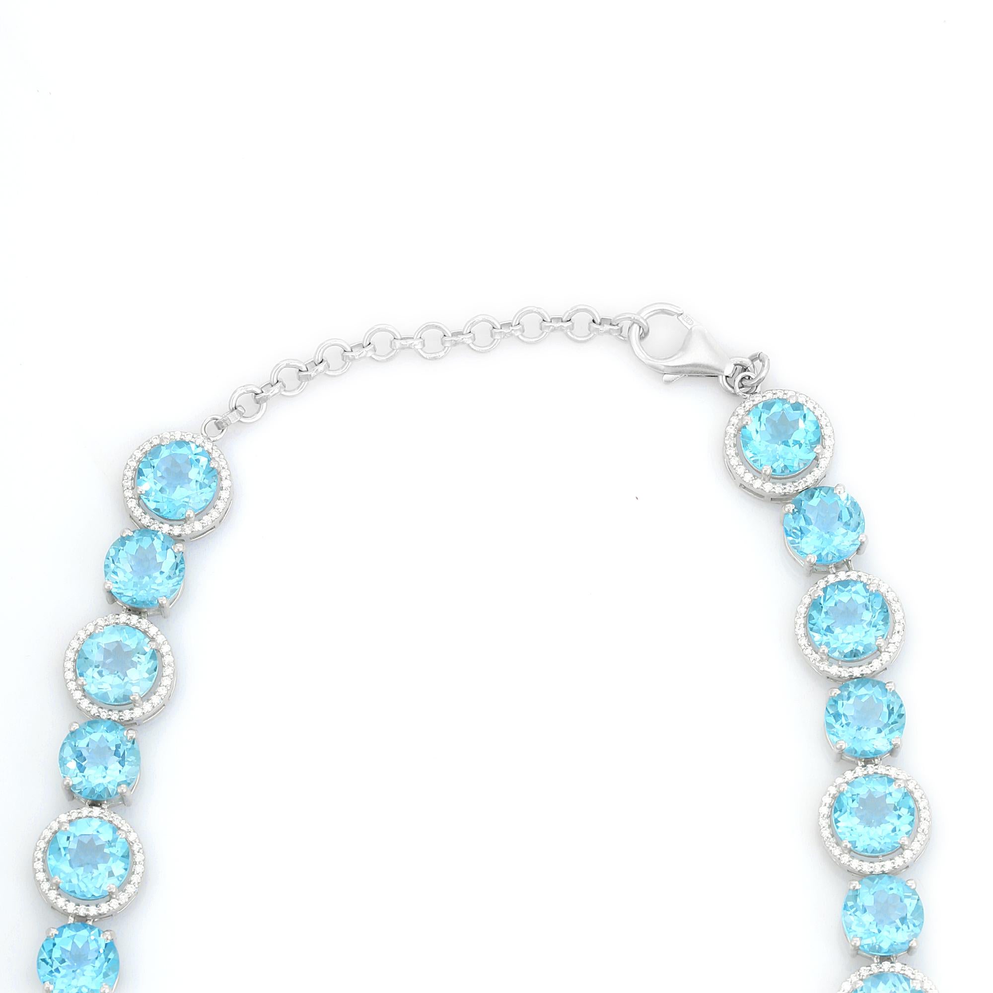 Este llamativo collar de plata con gemas de topacio azul y halo de circonitas está fabricado en plata de ley 925 y adornado con gemas de topacio azul brillantemente facetadas, cada una rodeada por un halo resplandeciente de circonitas cúbicas