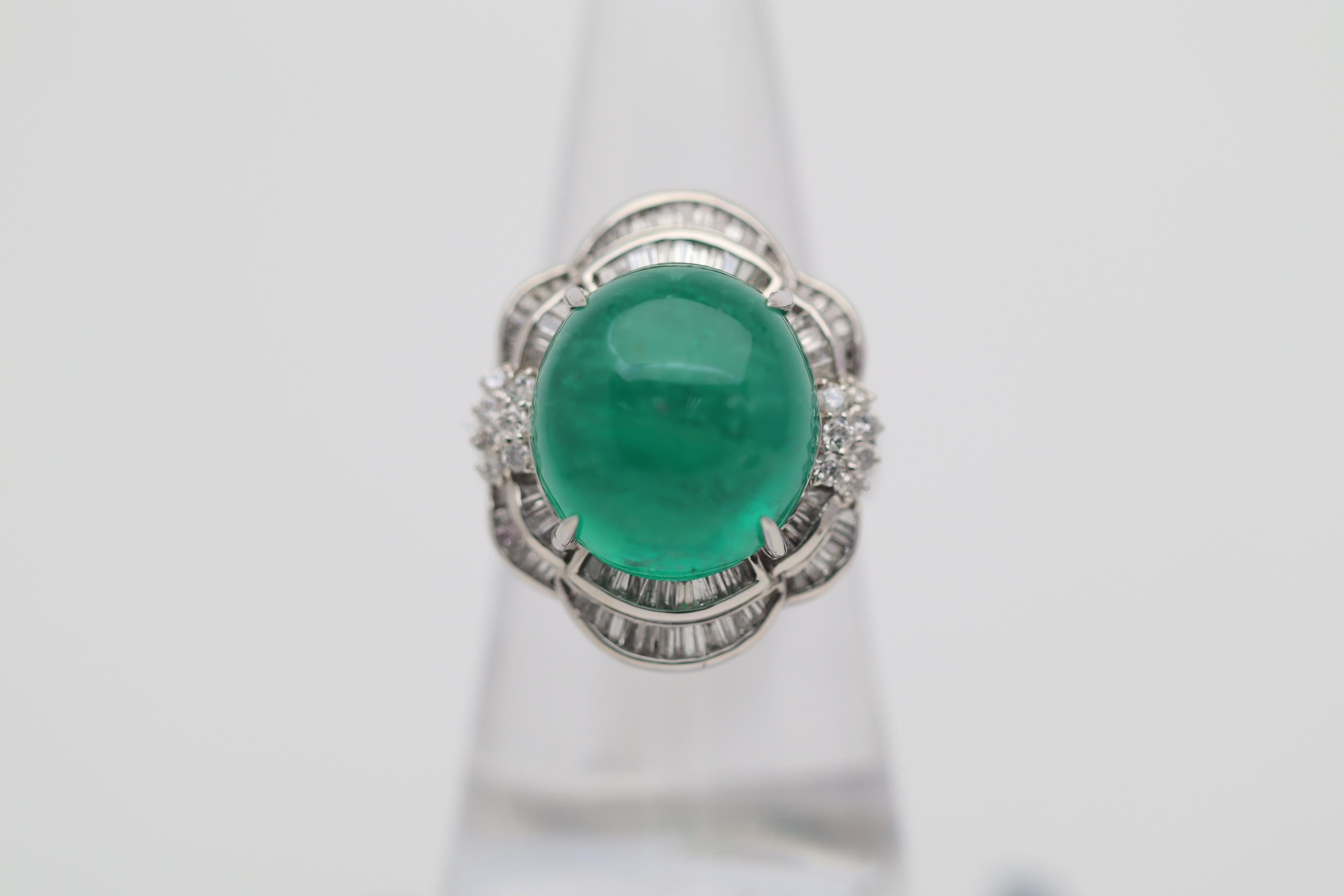 A large and impressive emerald weighing 13.65 carats takes center stage! It has a lovely rich grass green color along with a smooth cabochon domed finish. It is complemented by 1.08 carats of round brilliant and baguette-cut diamonds set around the