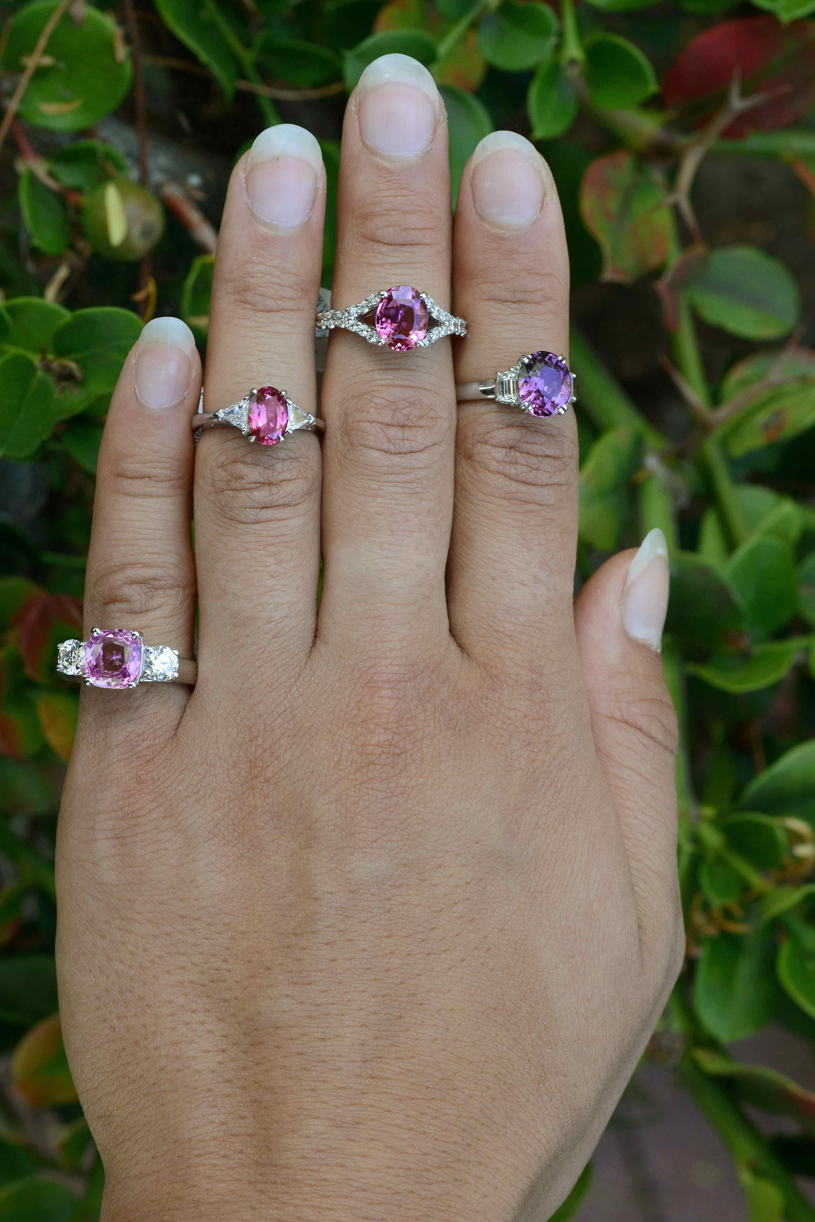 A most elegant natural pink sapphire 3 stone engagement ring. The ever-popular trinity design centered by a vivid, intense bubble gum pink sapphire, the oval cut bursting with a a most vibrant, shimmering shade with captivating brilliance. A vintage