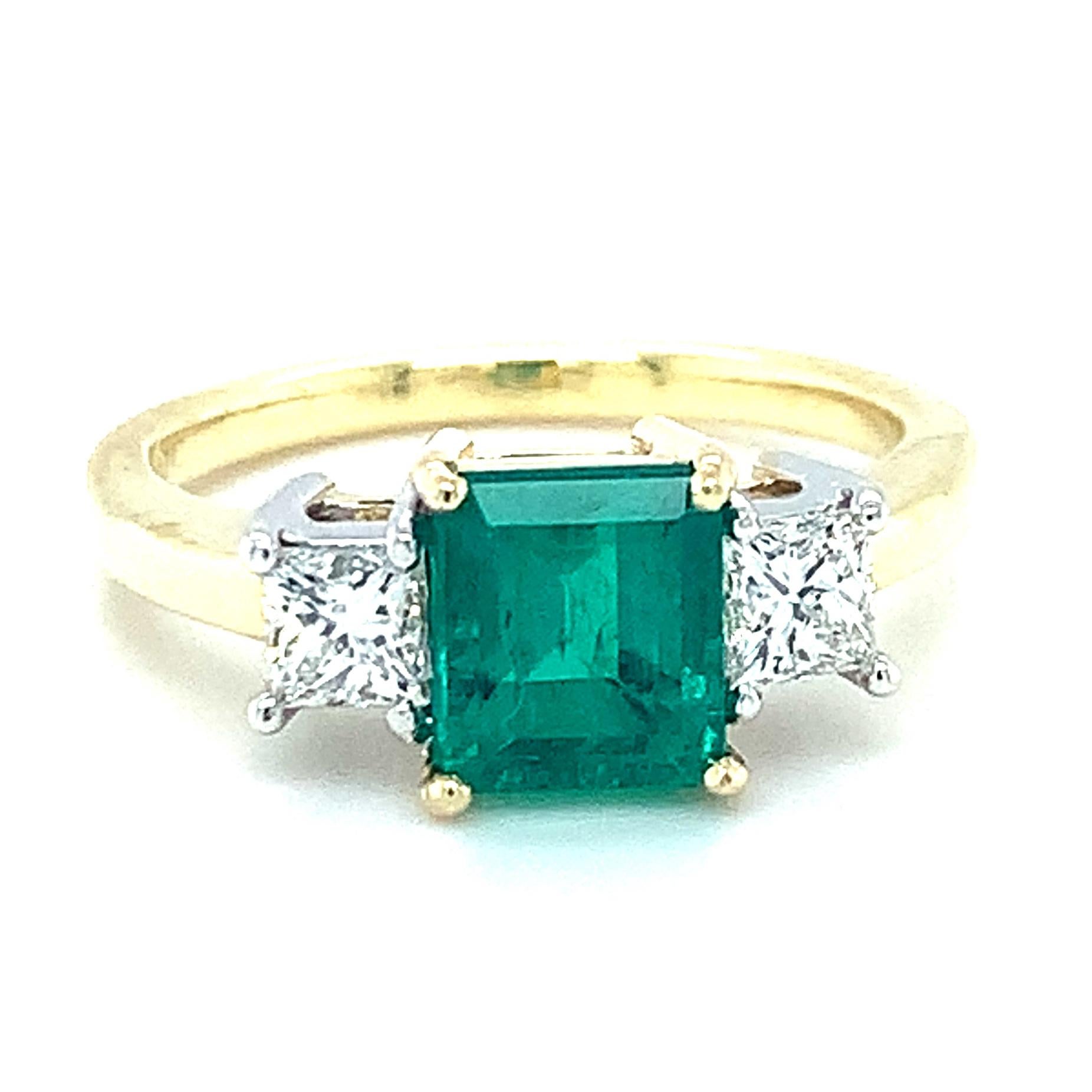 Digne d'envie ! Cette bague classique à trois pierres est ornée d'une magnifique émeraude verte qui possède une couleur et une brillance magnifiques. L'émeraude centrale est sertie dans de l'or jaune 18k, flanquée de diamants de taille princesse de