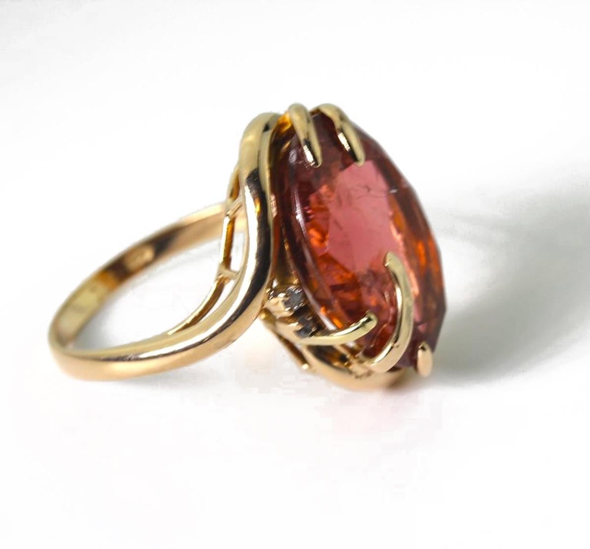 The glittering peachy red 13.82 carat Brasilian Tourmaline is enhanced with three teeny sparkling diamonds in a unique handmade 14Kt yellow gold ring size 7.  (sizable). The Tourmaline is 14mm x 18 mm.  More from this seller by putting gemjunky into