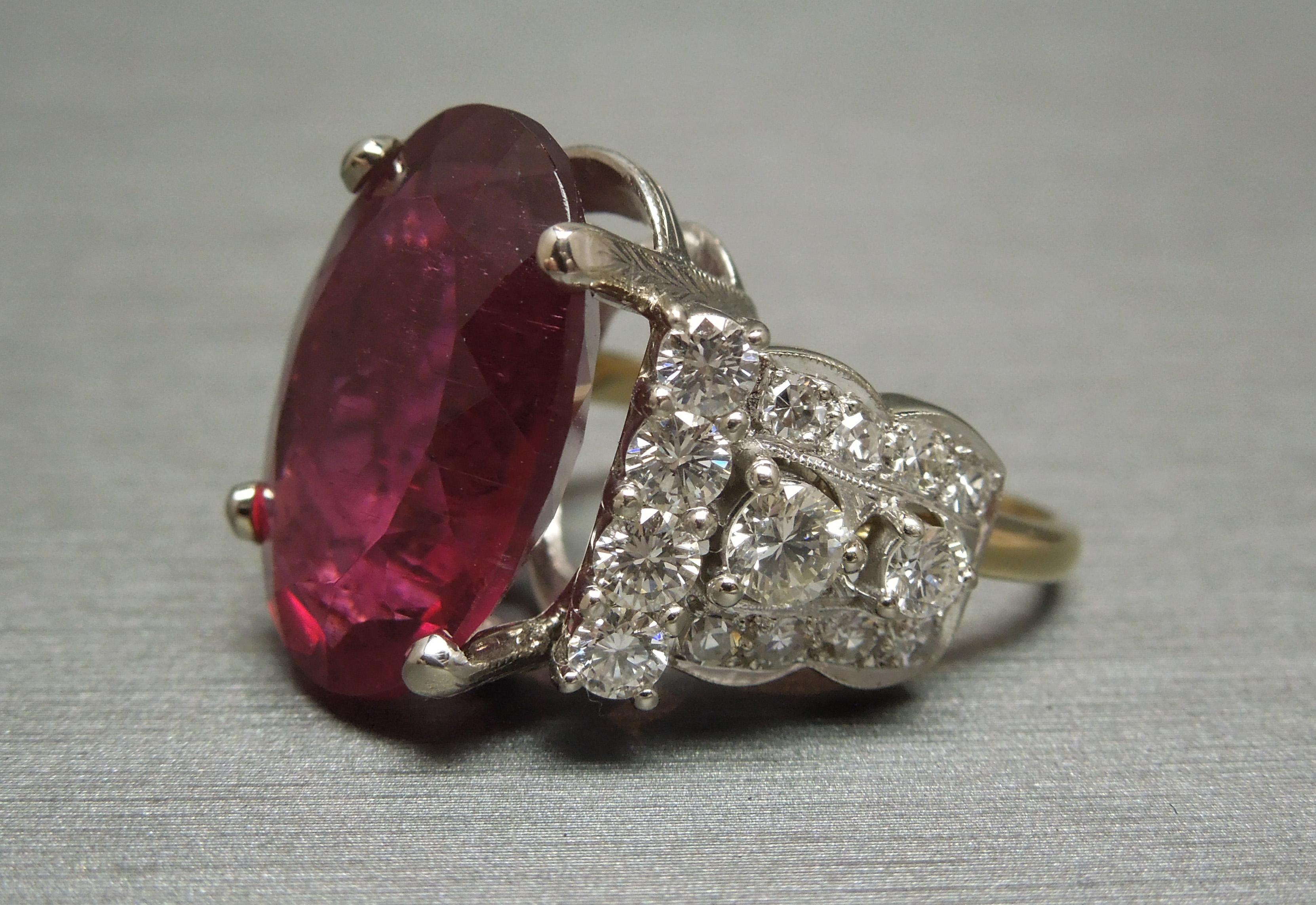 This Rubellite & Deco Diamond Ring features a central Brilliant Oval cut 13.84 carat GIA Certified Rubellite, a.k.a. Red Tourmaline, securely set in a 4-prong setting. Each prong accented with a Hand Engraved detailing as well. A vivid Red with deep