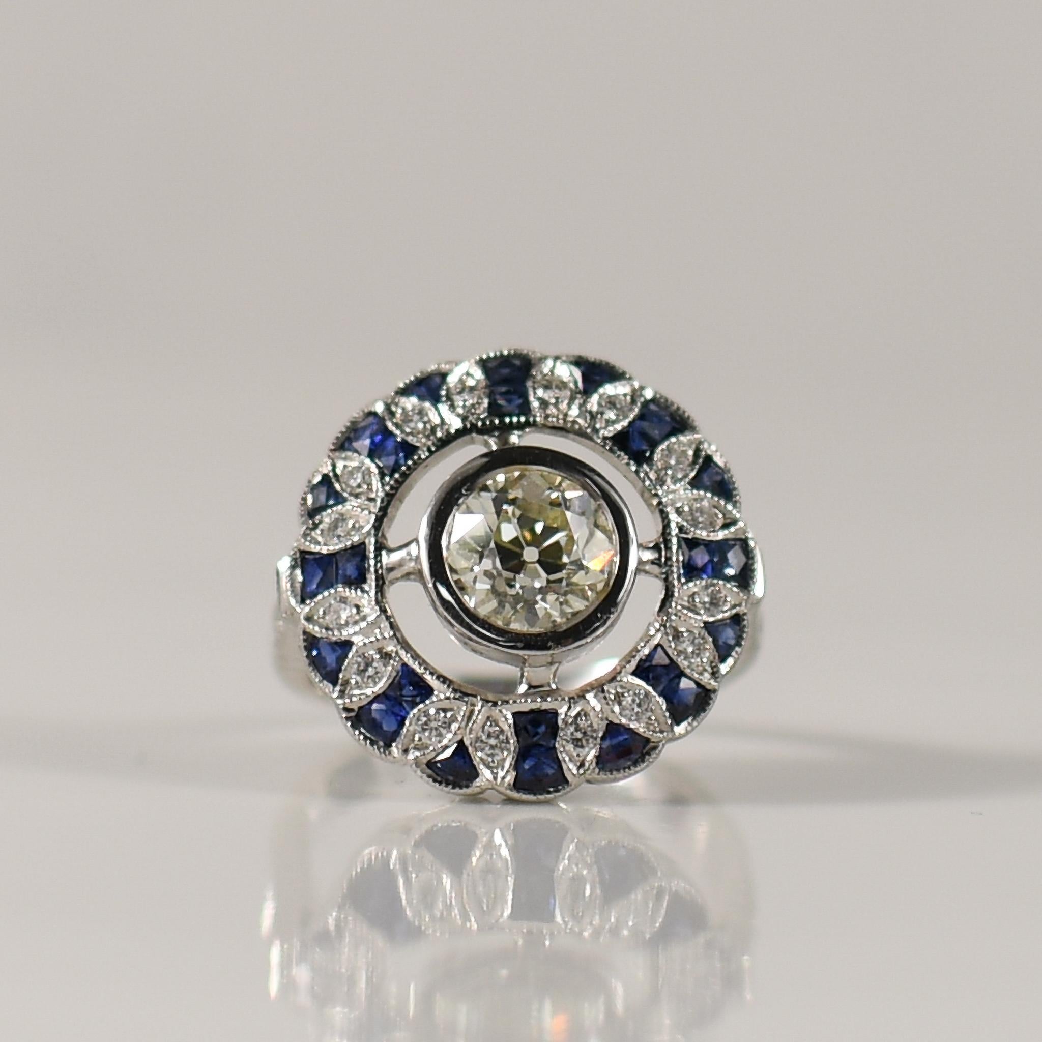 Step into the opulent world of the Roaring Twenties with this exquisite Art Deco inspired ring. Its focal point is a stunning 1.38 carat old European cut diamond, elegantly bezel set to exude timeless sophistication. Surrounding the center stone is