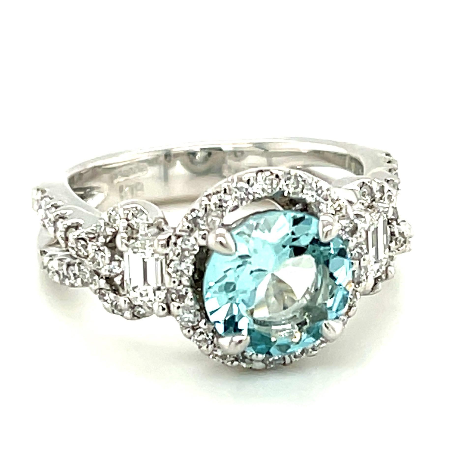 This eye-catching cocktail ring is set with a gorgeous round aquamarine of exceptional quality! The center gemstone is highlighted by a sparkling halo of brilliant white diamonds set in 18k white gold. Fine quality emerald-cut diamonds provide a