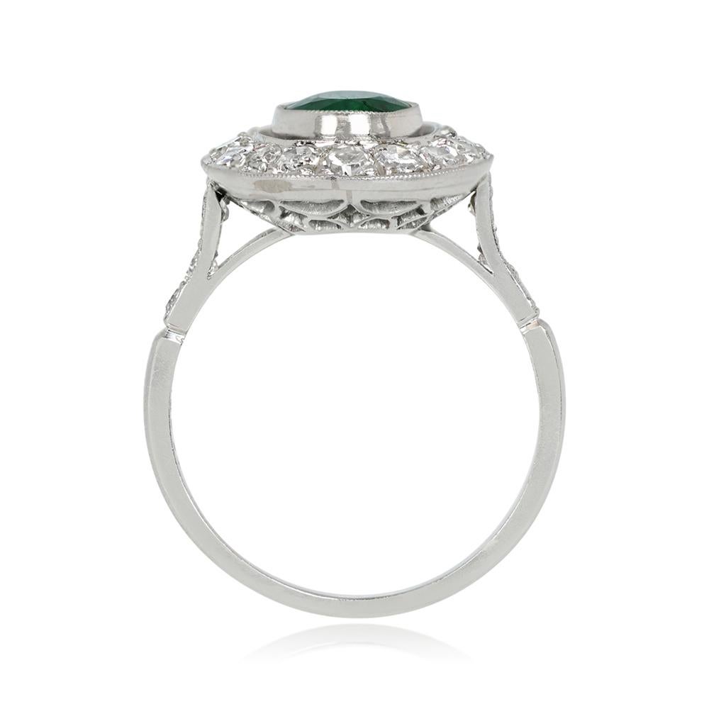 Presents a stunning ring featuring a 1.39-carat oval-cut natural emerald at its center. The emerald is bezel-set and framed by a halo of round-cut diamonds. Handcrafted in platinum, the mounting showcases intricate openwork in the under-gallery,