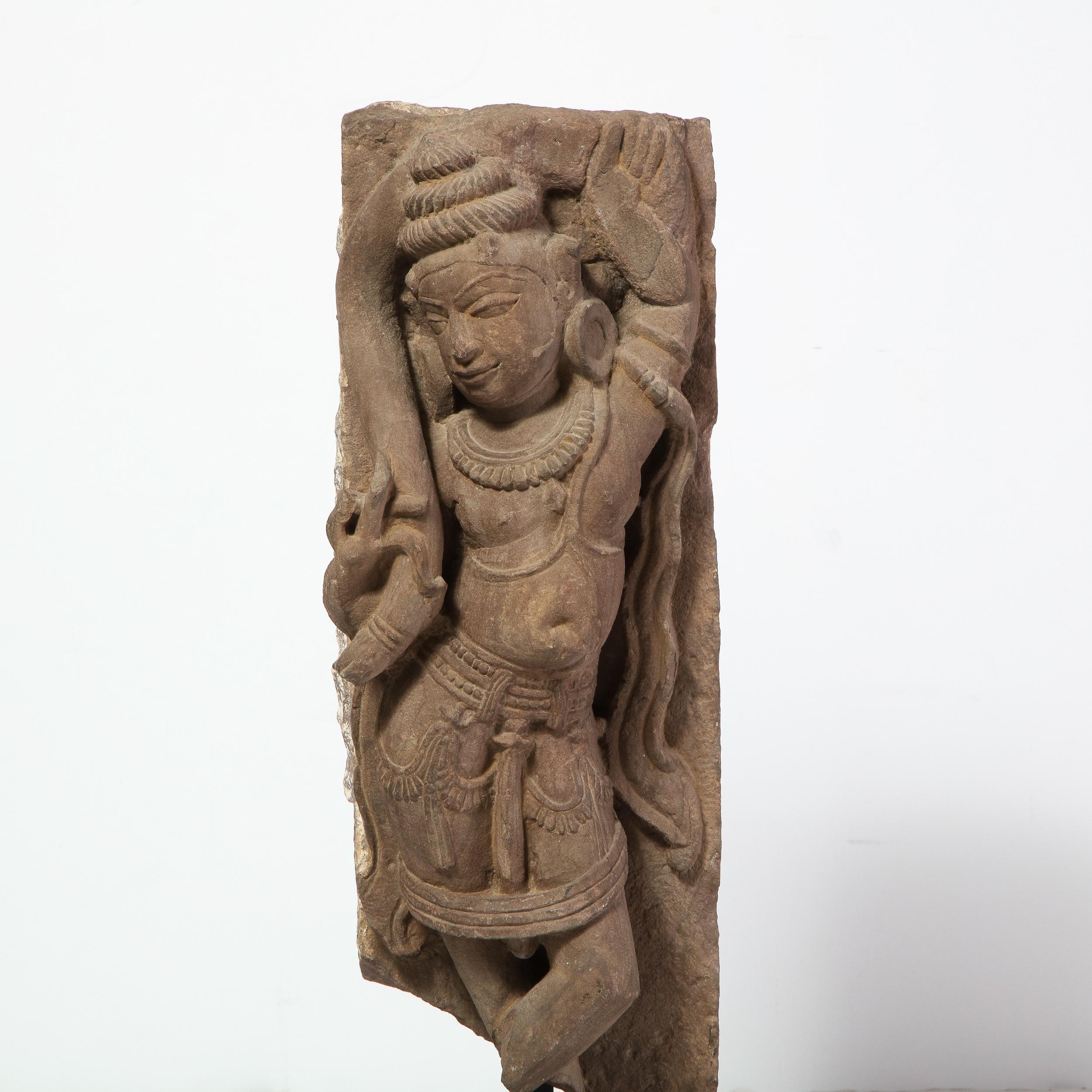 This stunning sandstone stele figure fragment was realized in India, during the 13th century. It offers an intricately carved Stele figure of a dancing goddess in sandstone. The female form appears to have her hips torqued and her legs subtly