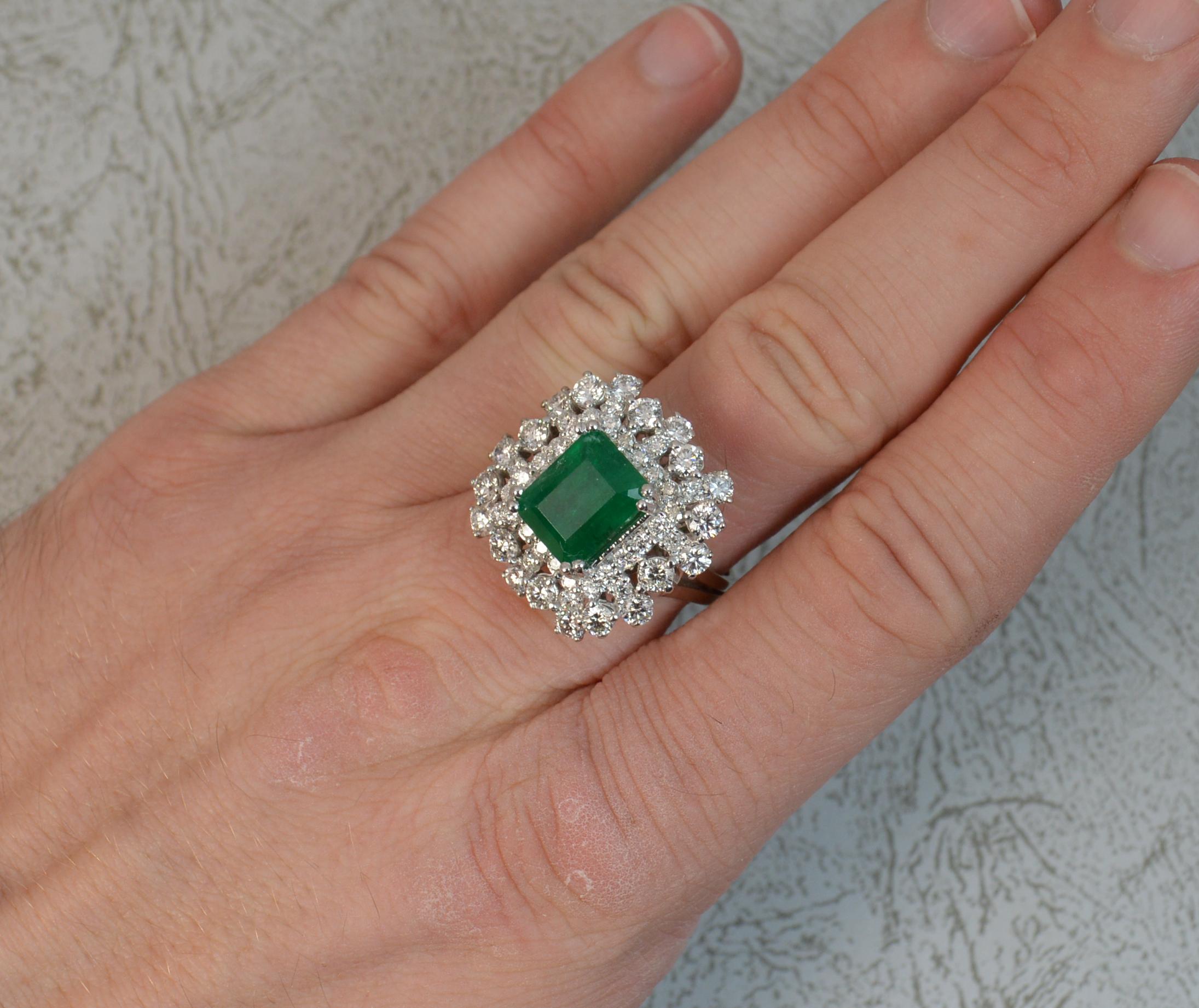 A superb 14ct White Gold, Emerald and Diamond cluster ring. A vintage piece of art deco design.
Designed with an emerald cut emerald to the centre in four double claw setting, 8.2mm x 10.3mm approx. 
Surrounding is multiple VS1 clarity, e-f colour