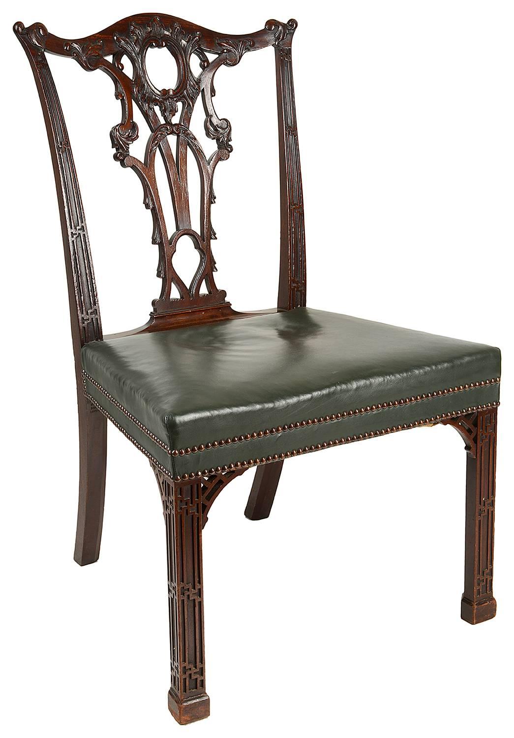 A fine quality set of 14 mahogany dining chairs in the Chippendale style (two later arms, 12 singles). Having carved scrolling foliate decoration to the backs, with gothic influenced blind fret work to the sides. Stuff over upholstered leather seats