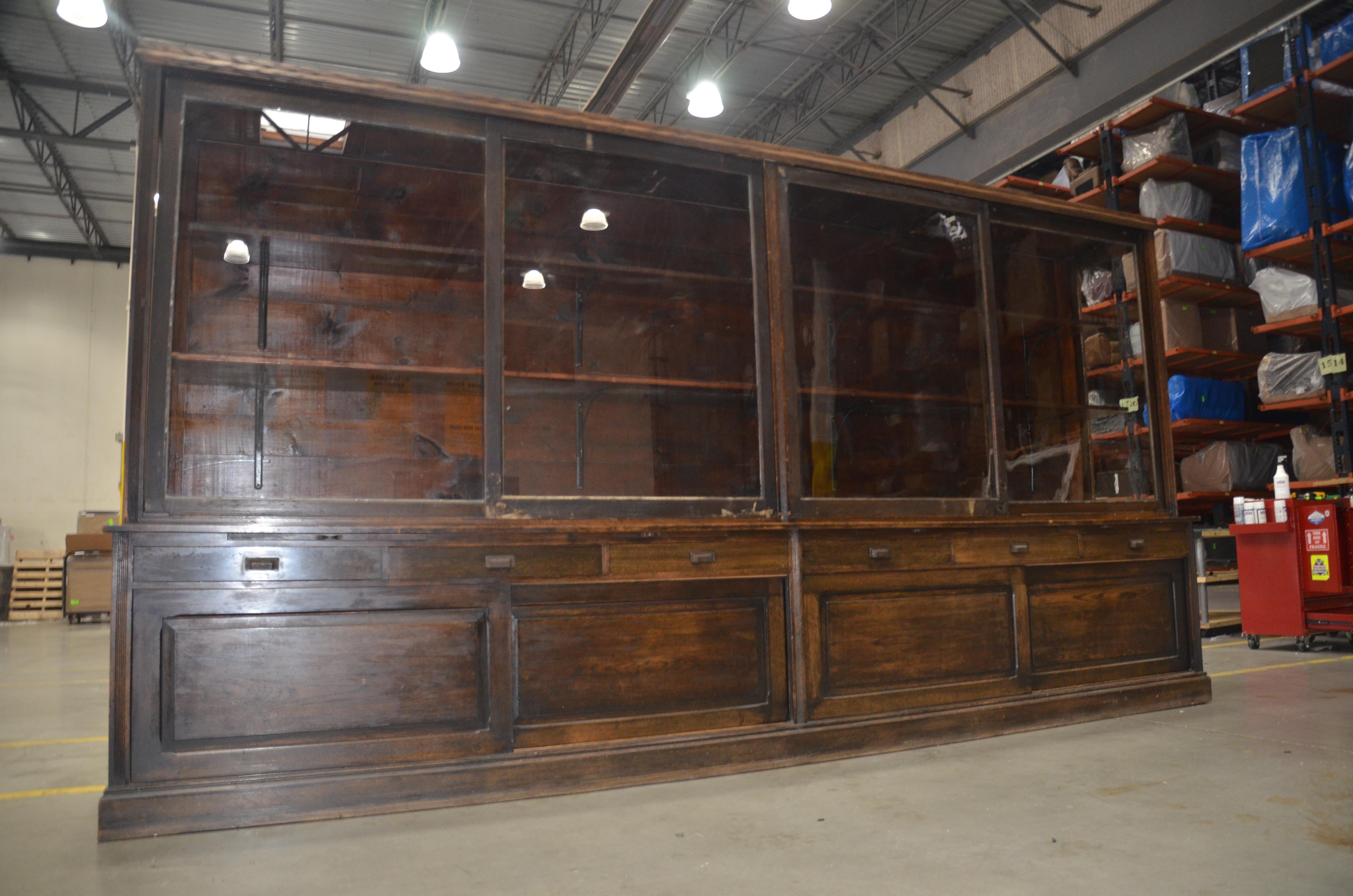 Impressive turn of the century oak wall cabinet that was formerly in a Midwestern general store. This large display cabinet measures 14 ft long. It features sliding glass doors on the top as well as sliding oak doors on the bottom. The center has