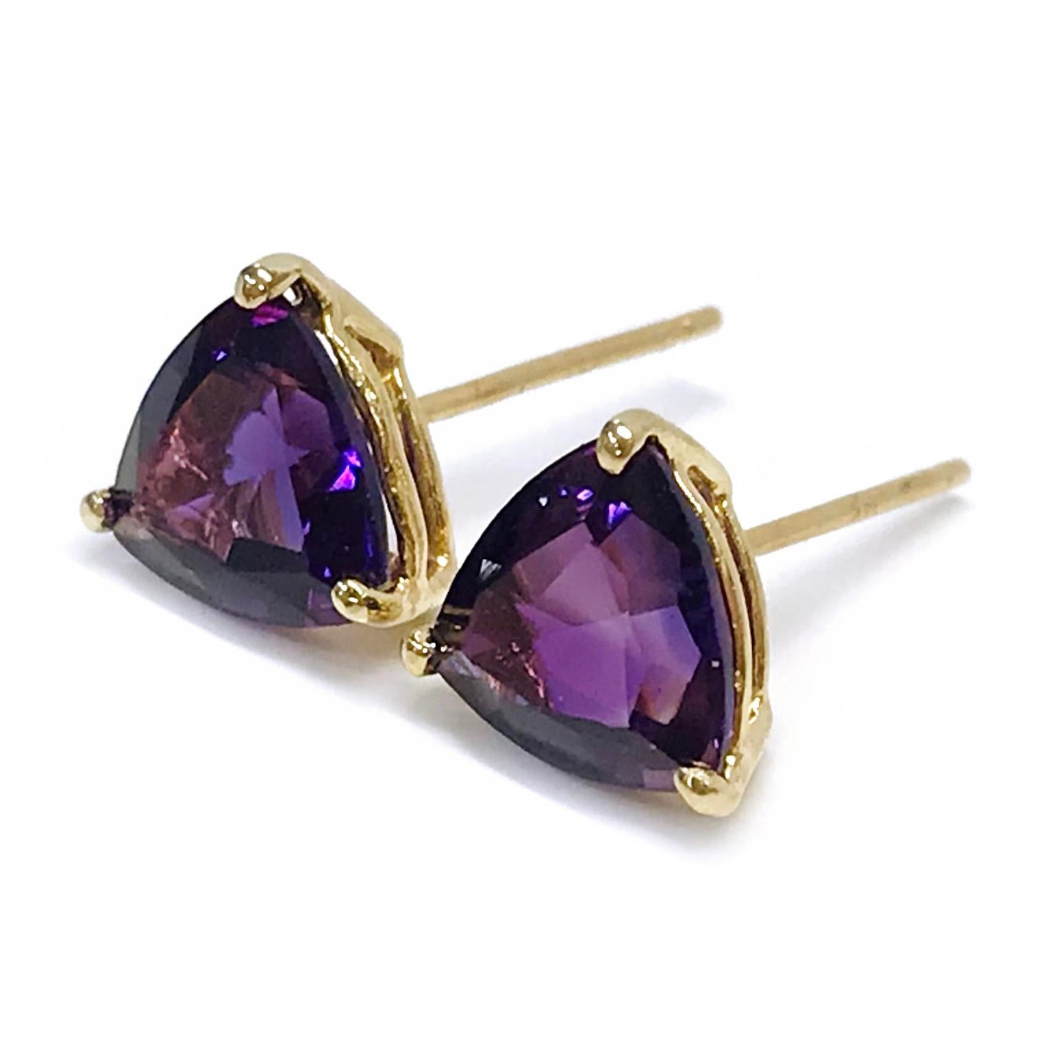 14 Karat Yellow Gold Amethyst Stud Earrings. The earrings each feature a 7 x 7mm trillion-cut Amethyst stone. The medium colored purple gemstones are three-prong-set.. The total weight of the earrings is 1.35 grams.