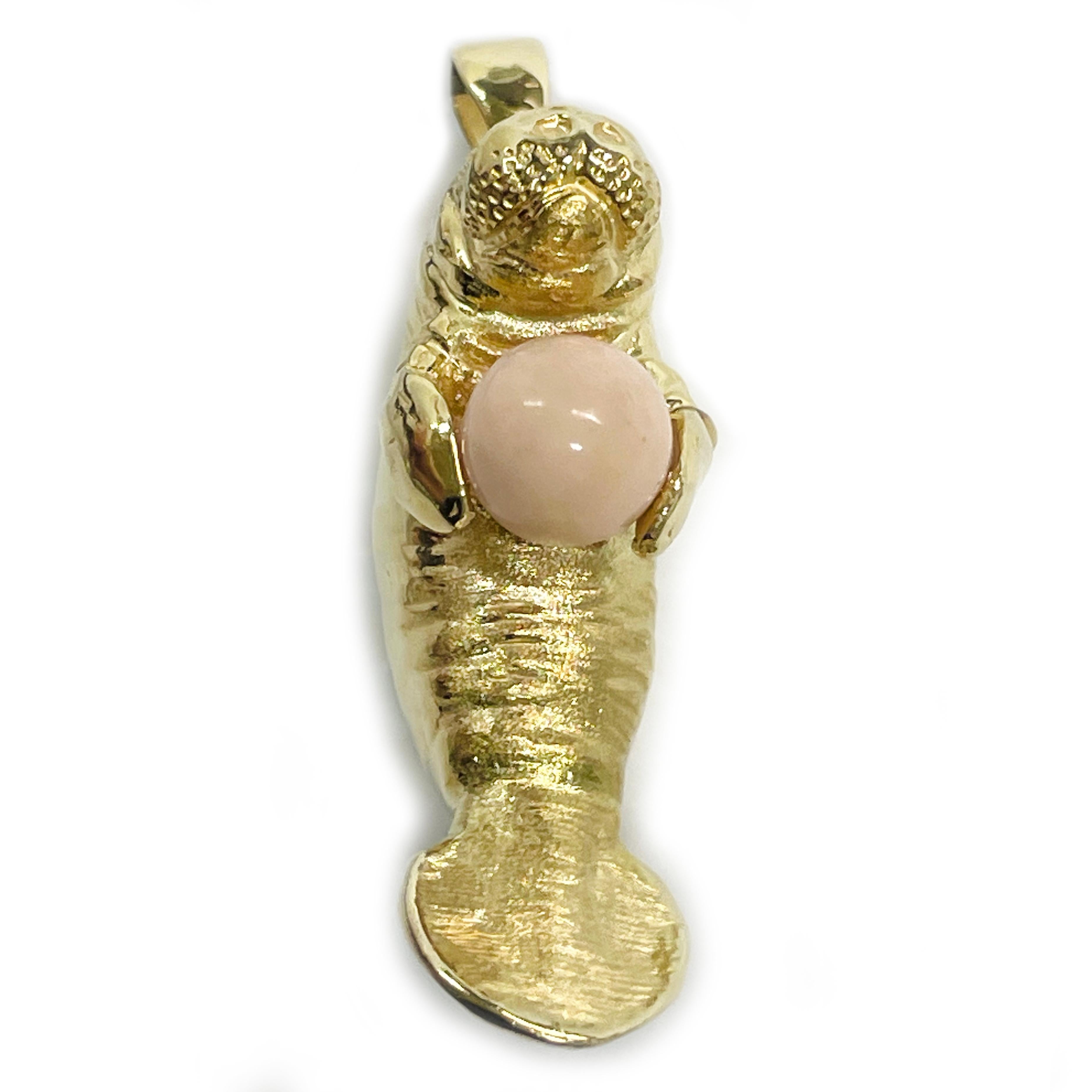 14 Karat Angel Skin Coral Manatee Pendant. This pendant features an adorable manatee holding an angel skin Coral bead. The round bead measures 9.14mm. The body of the Manatee has both a smooth and Florentine finish. The manatee measures 42.2 long x