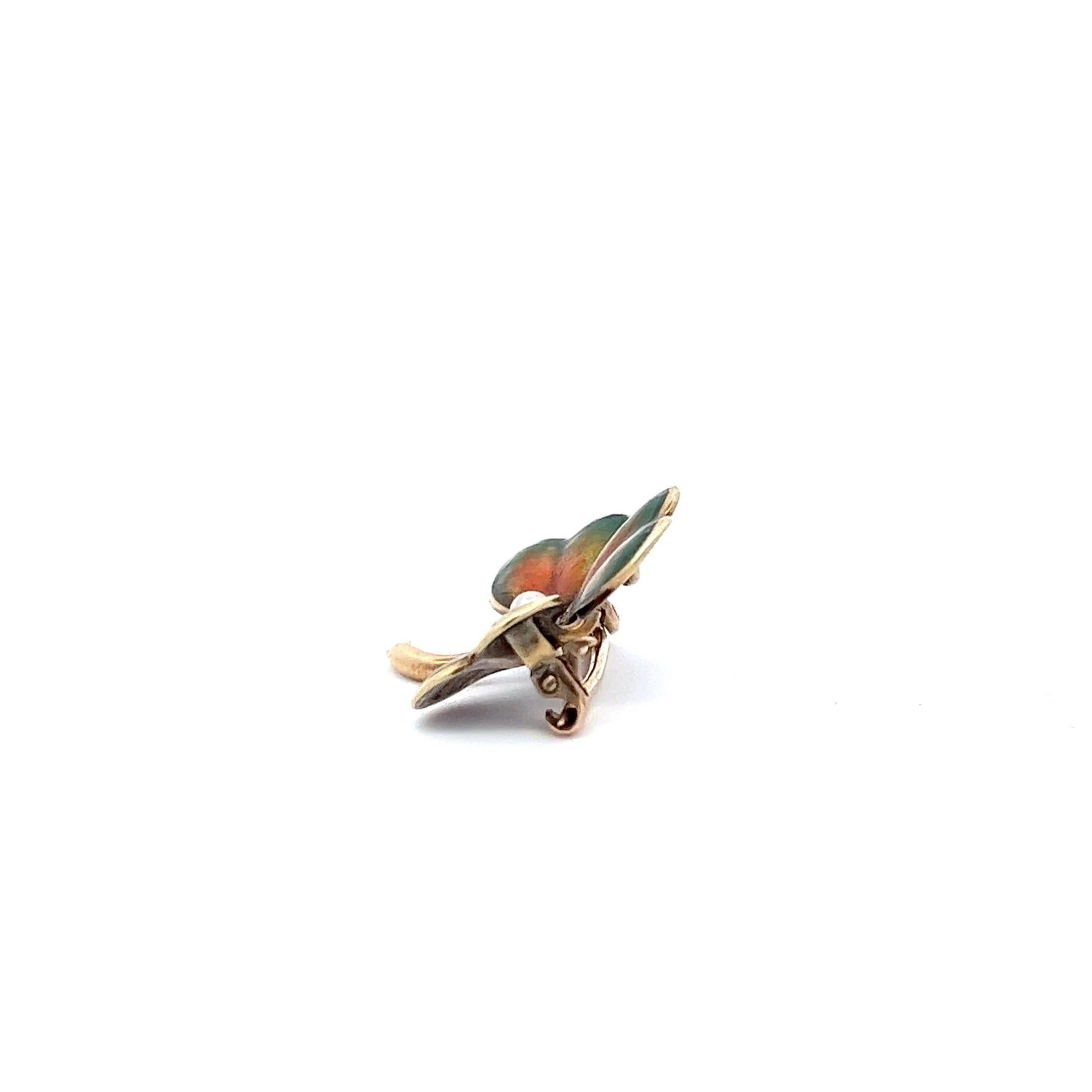 An exquisite example of Art Nouveau design, this clover-shaped brooch features a lustrous central pearl nestled among leaves detailed with a rich enamel palette. The skillful application of the enamel creates a seamless gradient of reds, greens, and