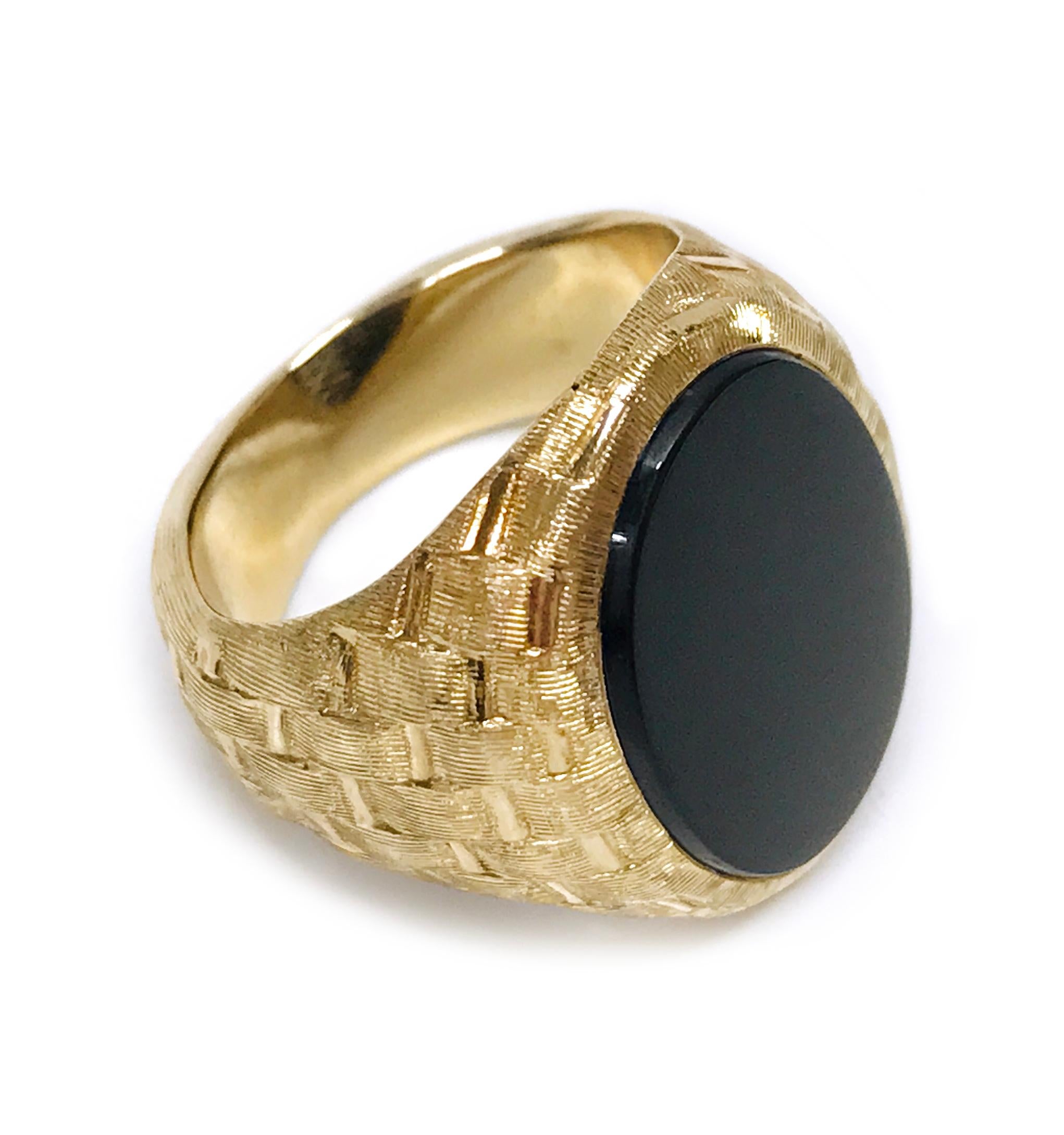 14 Karat Black Onyx Crosshatch Ring. The ring features a bezel-set flat oval black onyx cabochon. The Onyx is 18 x 13mm and the ring size is 5 1/2. The wide band tapers and the gold has a basket weave style finish all around. The total gold weight