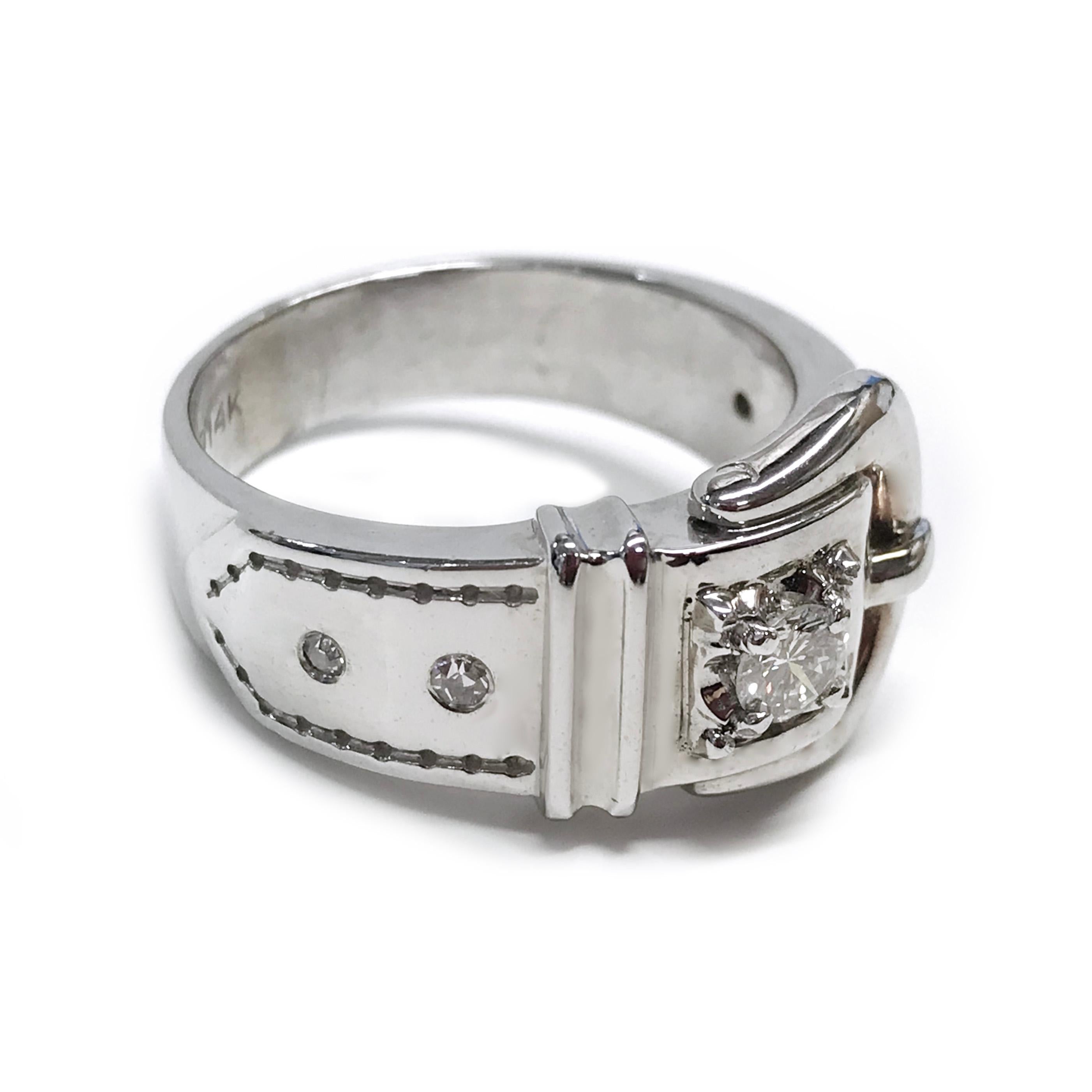 14 Karat White Gold Buckle Diamond ring. The ring features a belt buckle design with a four prong-set center diamond and four smaller side diamonds flush-set along the band. The round center diamond has a total carat weight of 0.25ct, the smaller