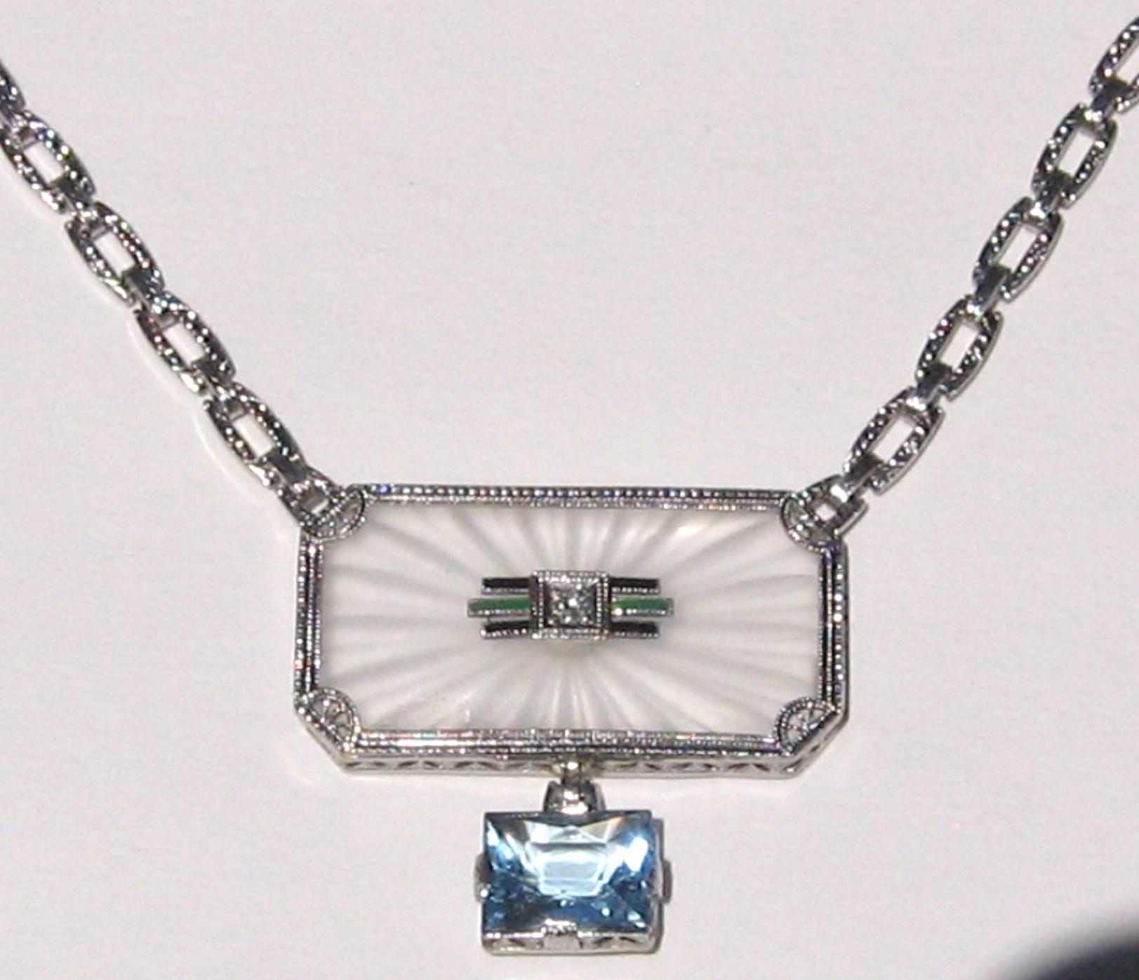 This is truly a stunning 14k White Gold Camphor Glass necklace. It has a center accent diamond with enameling surrounding it. There a 2.2 Carat aquamarine dangling down. The chain on this is also stunning. Measuring 17 in. end to end. What a