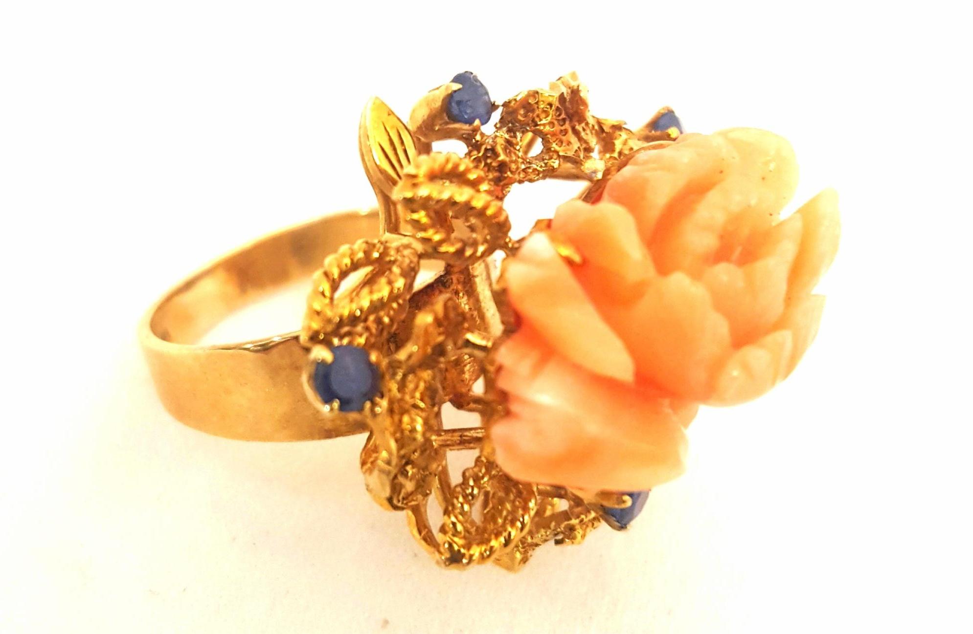 Different and Delightful!  This 14 karat yellow gold ring features a carved, lifelike blooming flower as the focal point.  Seven beautifully matched round faceted prong set sapphires add elegance and interest.  Twisted wire open work leaves and flat