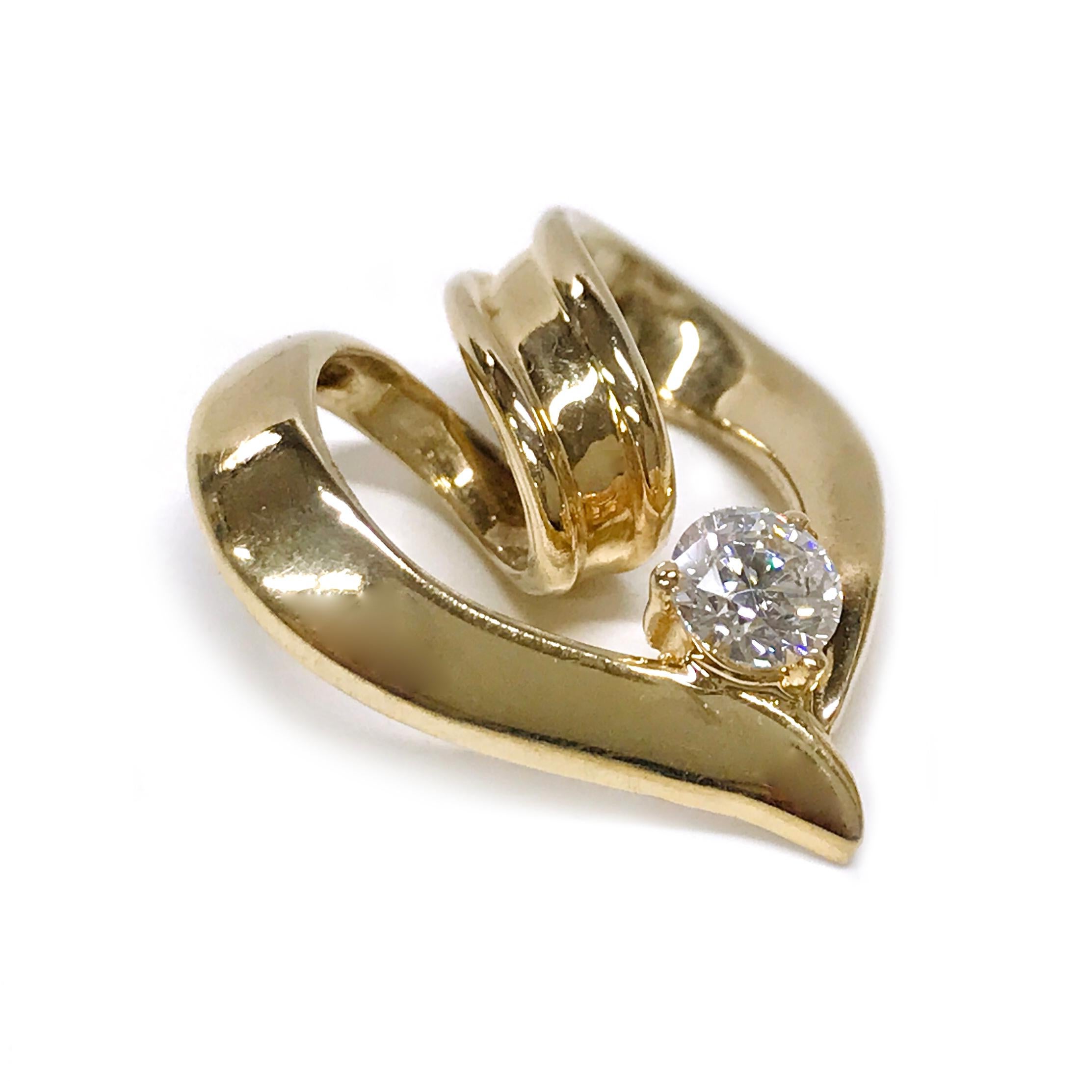 14 Karat Diamond Heart Slide Pendant. A single round diamond is a three-prong set in yellow gold on the bottom center of the heart where the curves meet. The heart is created by two ribbon-like gold swirls. The diamond measures 4.3mm and has a total