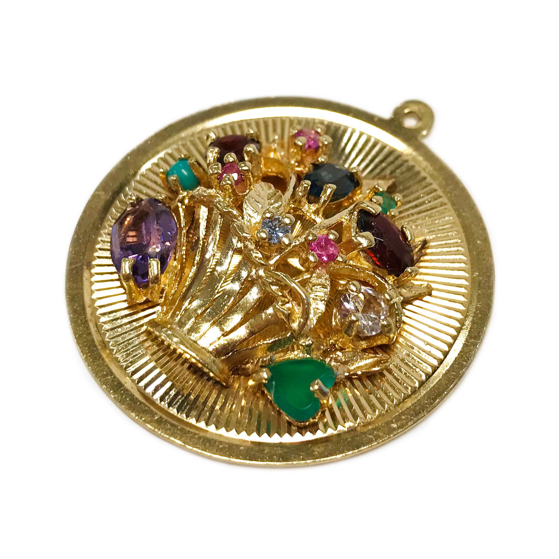 14 Karat Flower Basket Multi-Stone Medallion Pendant. The pendant measures 34.5mm in diameter. The pendant has a radial linear texture with a gold basket, gold leaves, and multiple gemstones in varying colors, sizes, and shapes, all prong-set. There