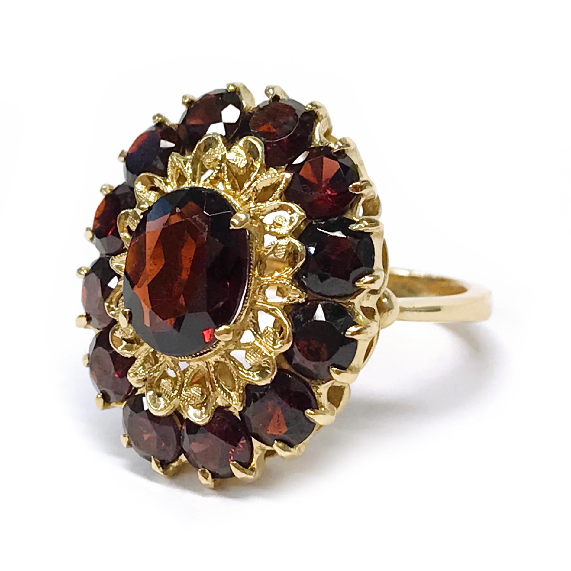 18 Karat Garnet Cluster Ring. This cocktail ring features an oval Garnet at the center with twelve round garnets prong-set around it. The center Garnet measures 10mm x 8mm. The surrounding Garnets measure 4.2mm each. The ring size is 7 1/4. Stamped