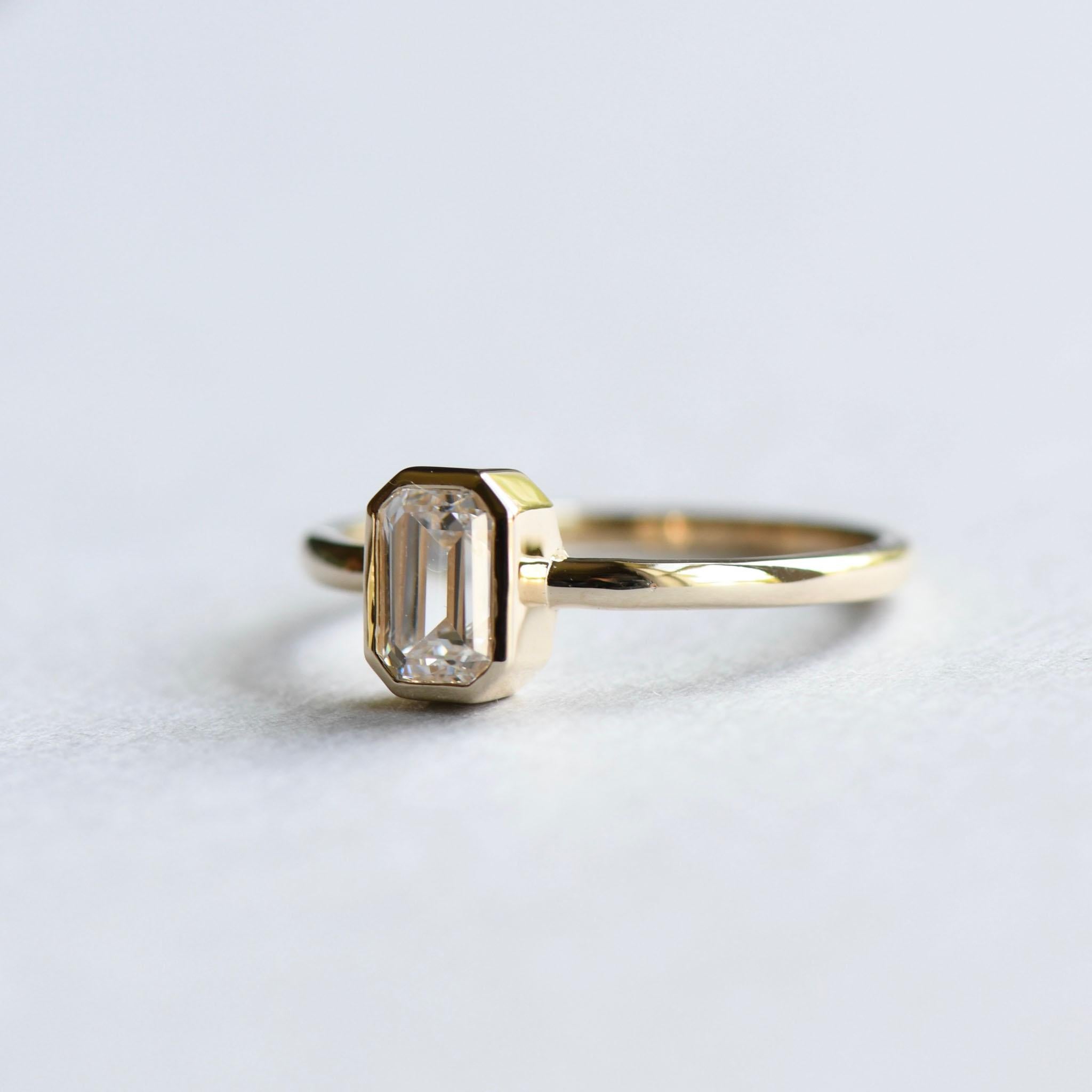 Bezel set emerald cut moissanite engagement ring set on 18 karat yellow gold. 
Stone: Moissanite Forever One by Charles and Colvard and each stone comes with an authenticity/warranty card
Stone Shape: Emerald
Cut: Step cut
Color: Colorless