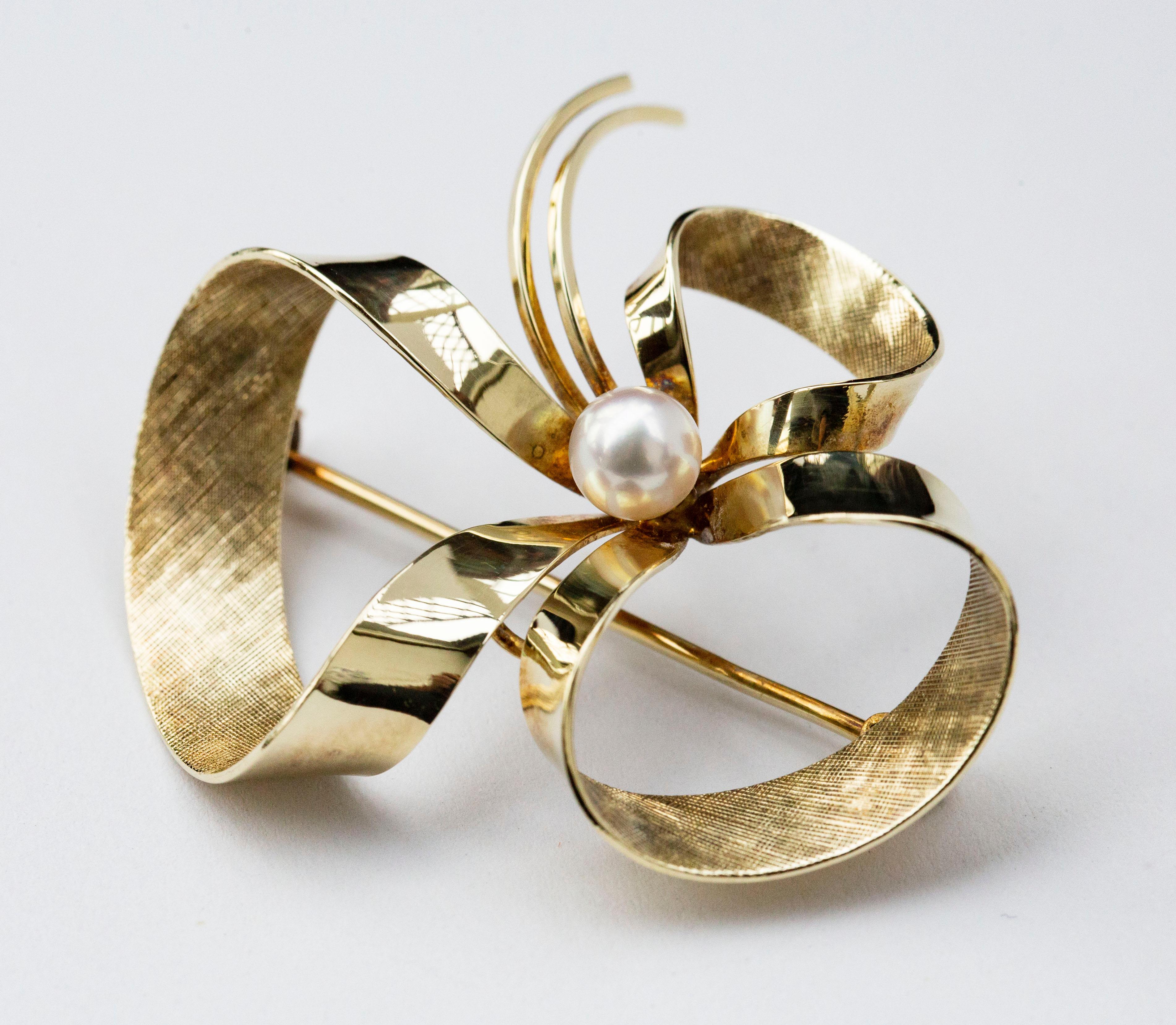 A vintage bow brooch crafted in 14 karat yellow gold. The outside surface of the bow is made of smooth gold while the inner surface is textured and matted. The brooch is set with a cultured pearl in the centre. The brooch closes with a roll-over