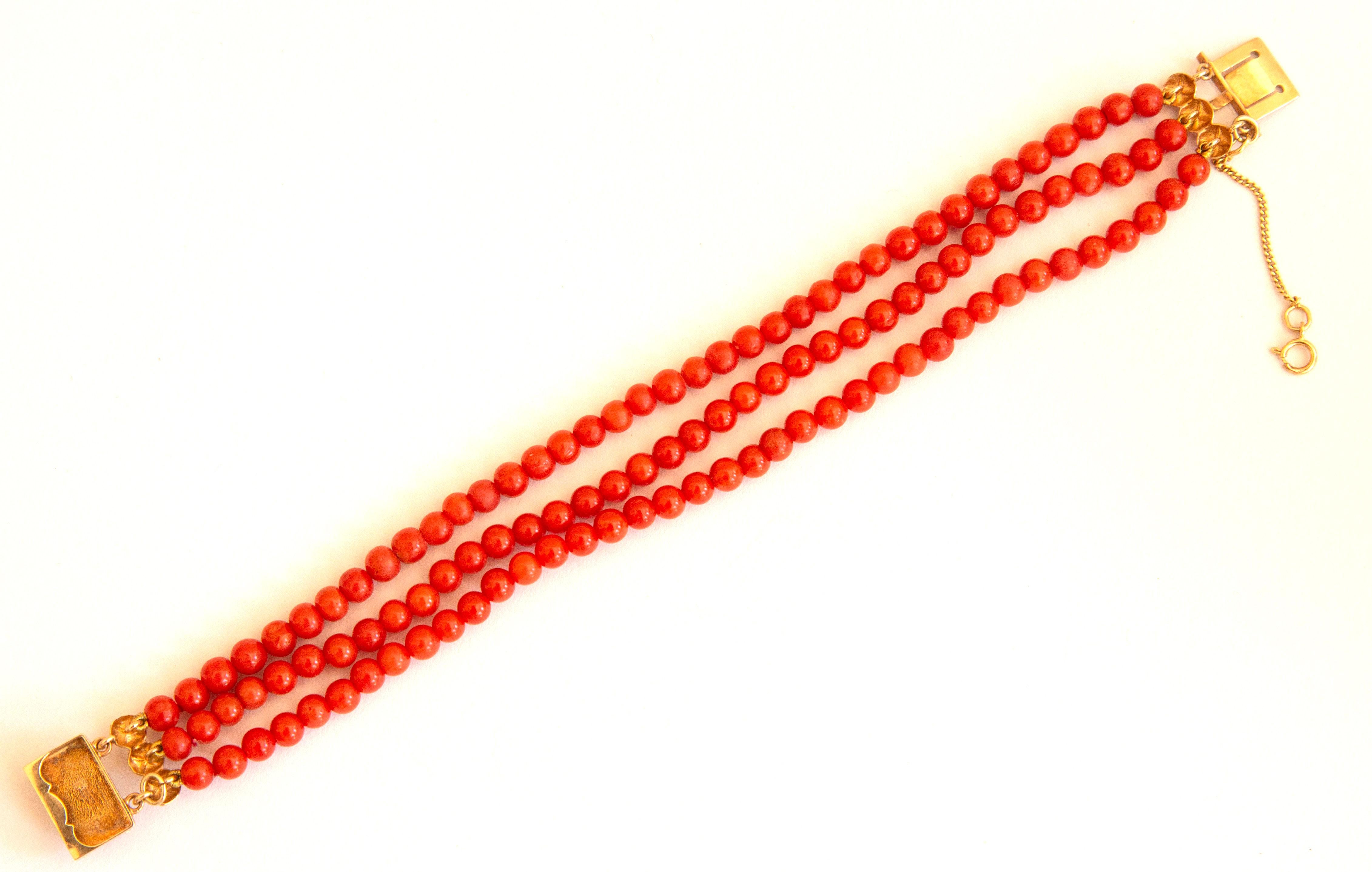 An antique bracelet made of natural red coral beads with 14 karat golden clasp. The bracelet features three strands of round - shaped beads. The diameter of the beads is ca. 5 mm and the color is red. The clasp features a rectangular shape with two